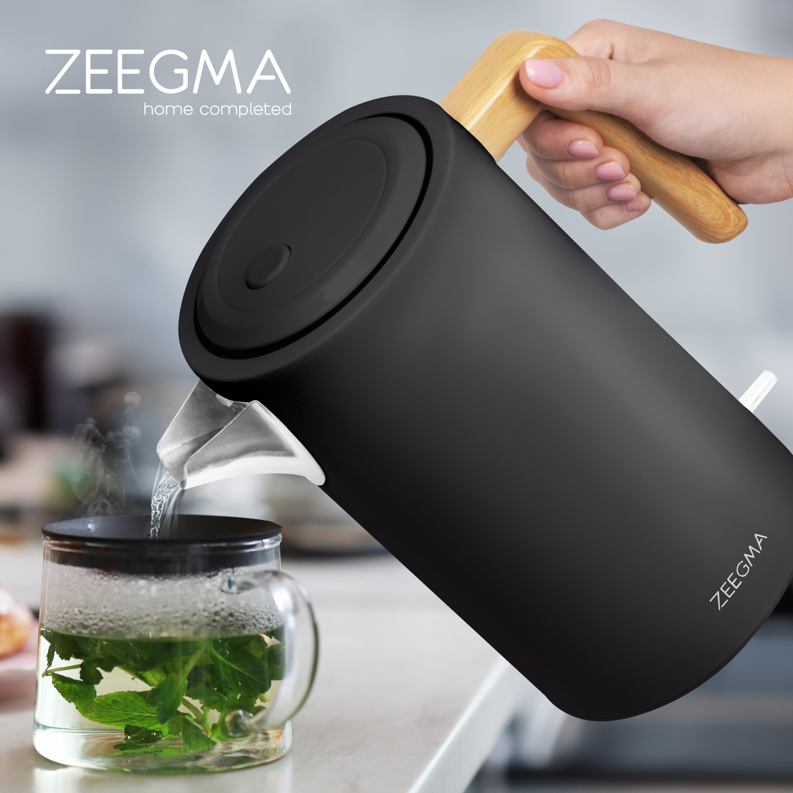 Osoba nalewa wodę do szklanki z miętą. Czarny czajnik z drewnianym uchwytem. Logo Zeegma.