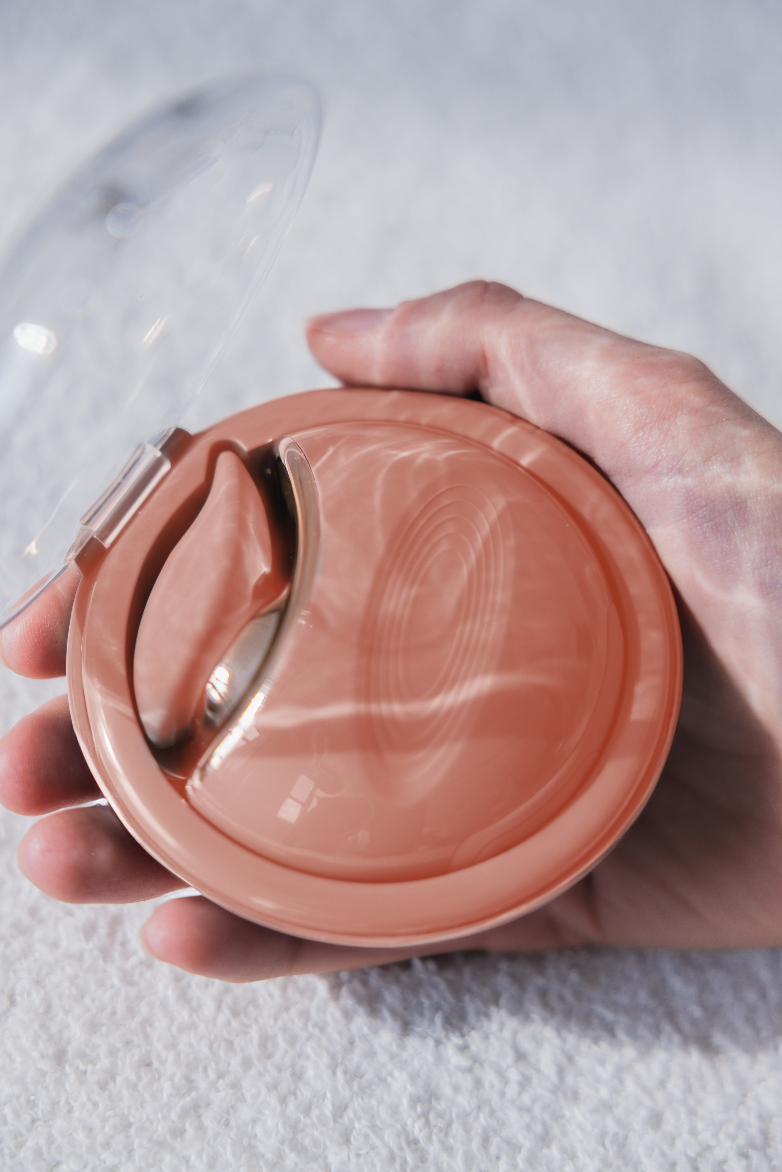 Eine Hand, die einen runden, pfirsichfarbenen Behälter mit zwei Gelpads darin hält. Der Behälter ist offen.