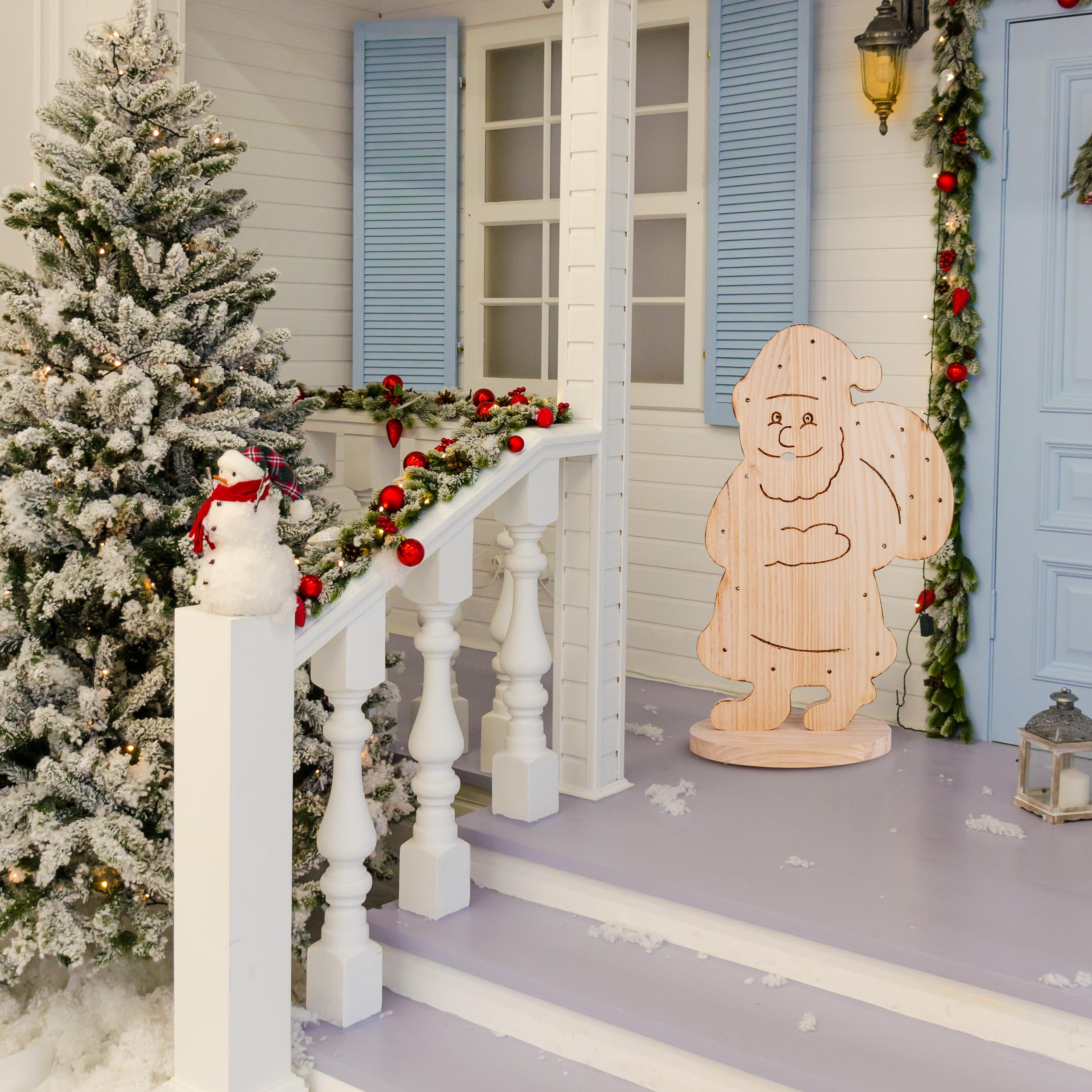 Eine Weihnachtsszene vor einem Haus. Weihnachtsbaum, Schneemann und Santa-Ausschnitt auf der Veranda.