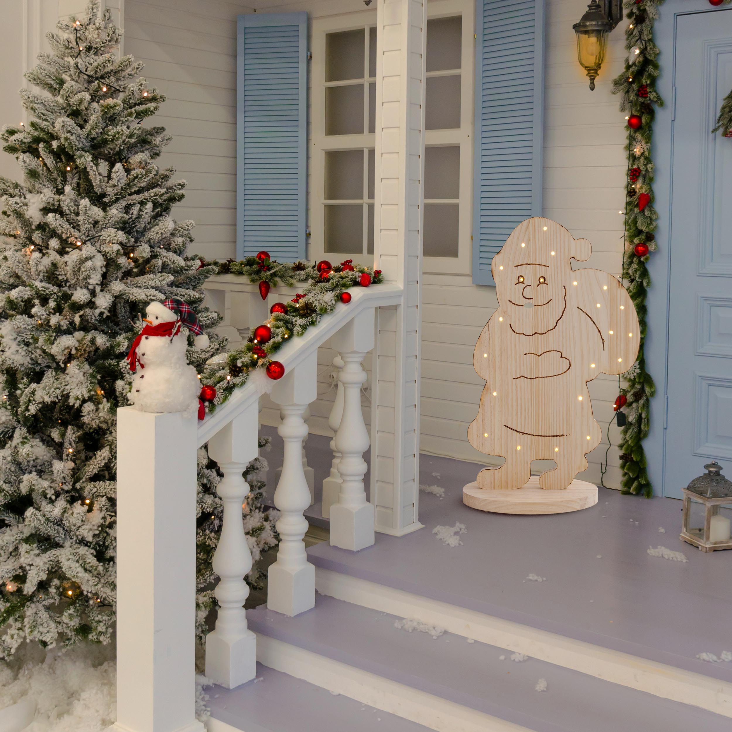 Weihnachtsdekorationen auf einer Veranda mit Schnee und einem Holz-Weihnachtsmann.