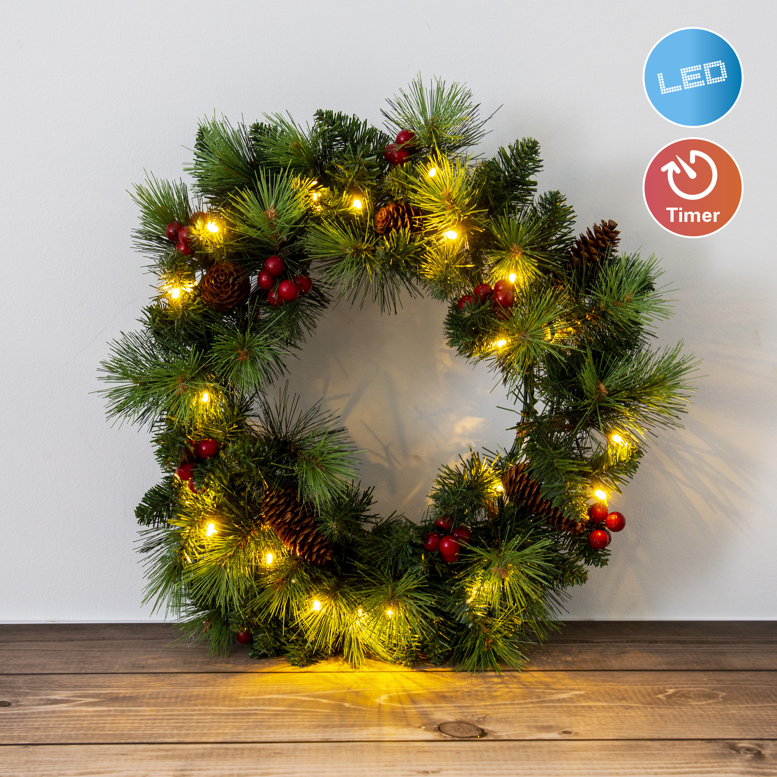 Ein Weihnachtskranz mit Lichtern und Beeren auf Holz und einer weißen Wand.