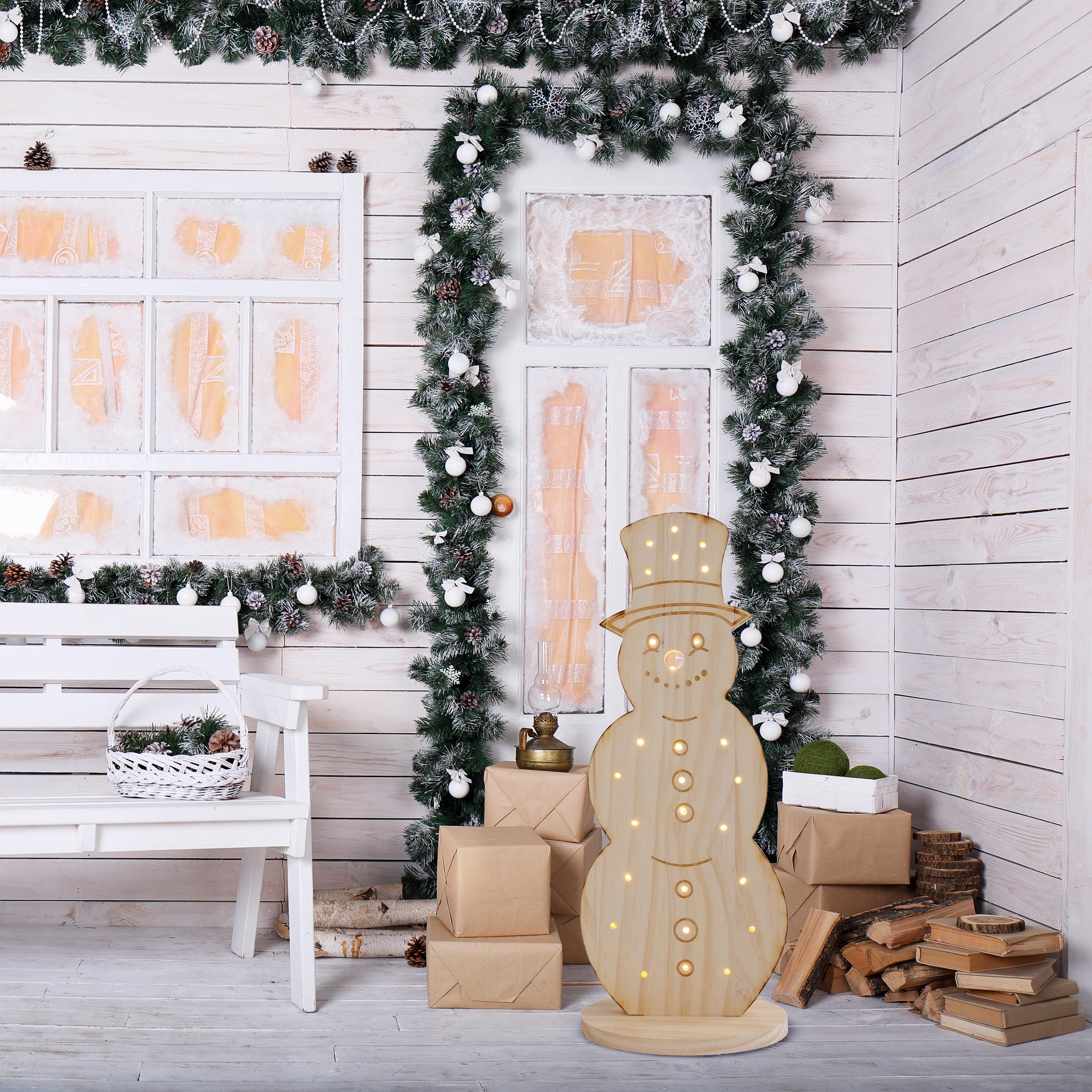 Schneemann-Dekoration aus Holz mit Lichtern und Hut. Vor einer weißen Holzwand.