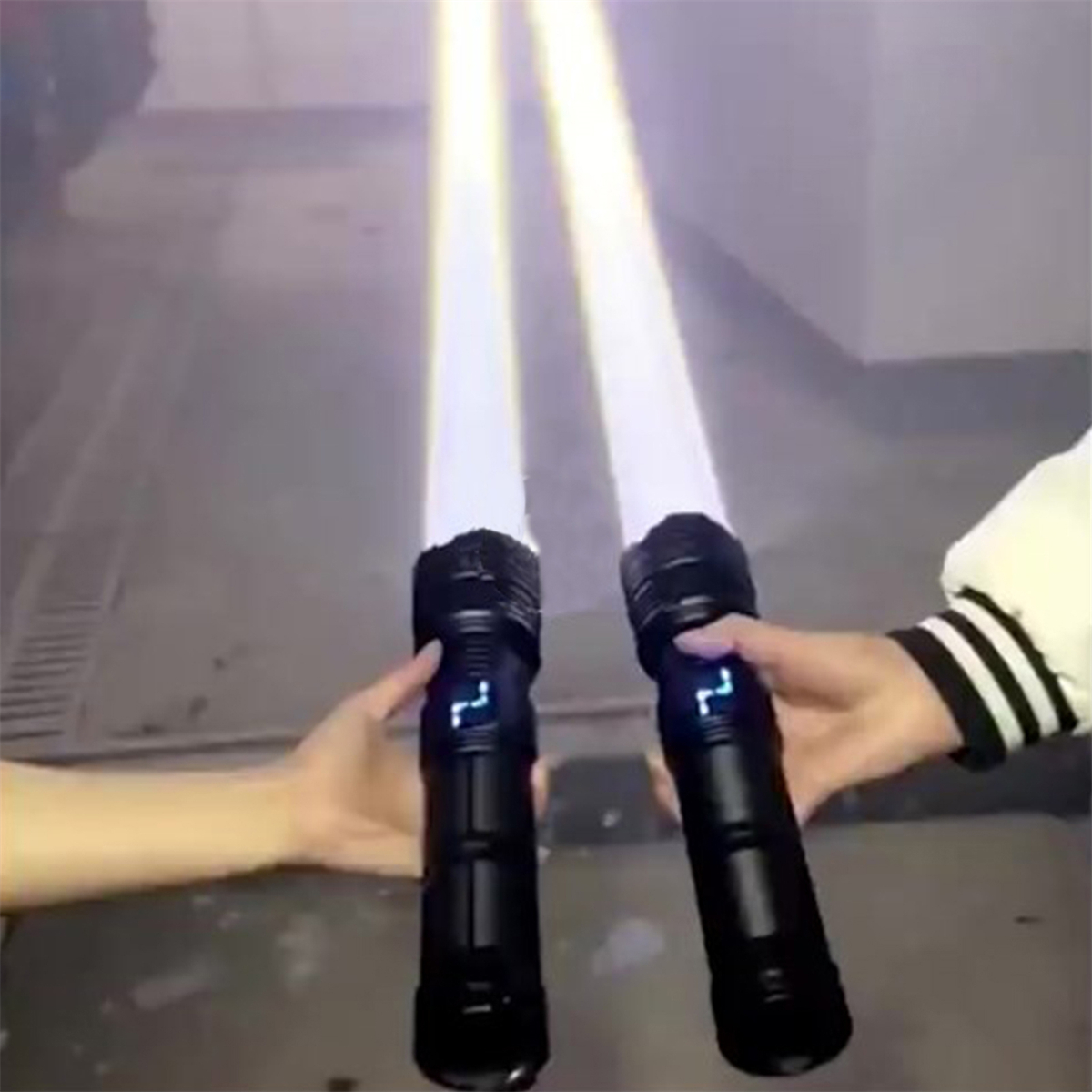 Zwei schwarze Lichtschwerter mit weißen Klingen werden von Händen vor grauem Hintergrund gehalten.
