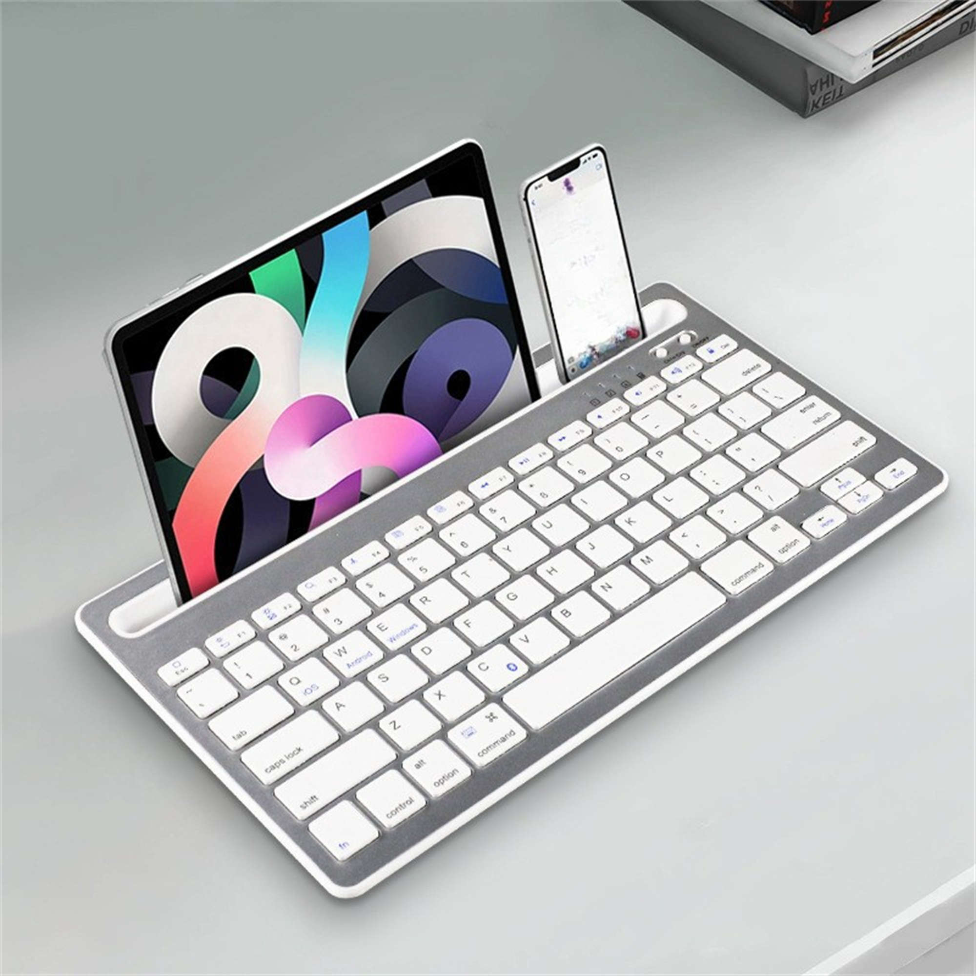 Silberne Tastatur mit Tablet und Telefon in den Ständern, auf hellgrauer Oberfläche.