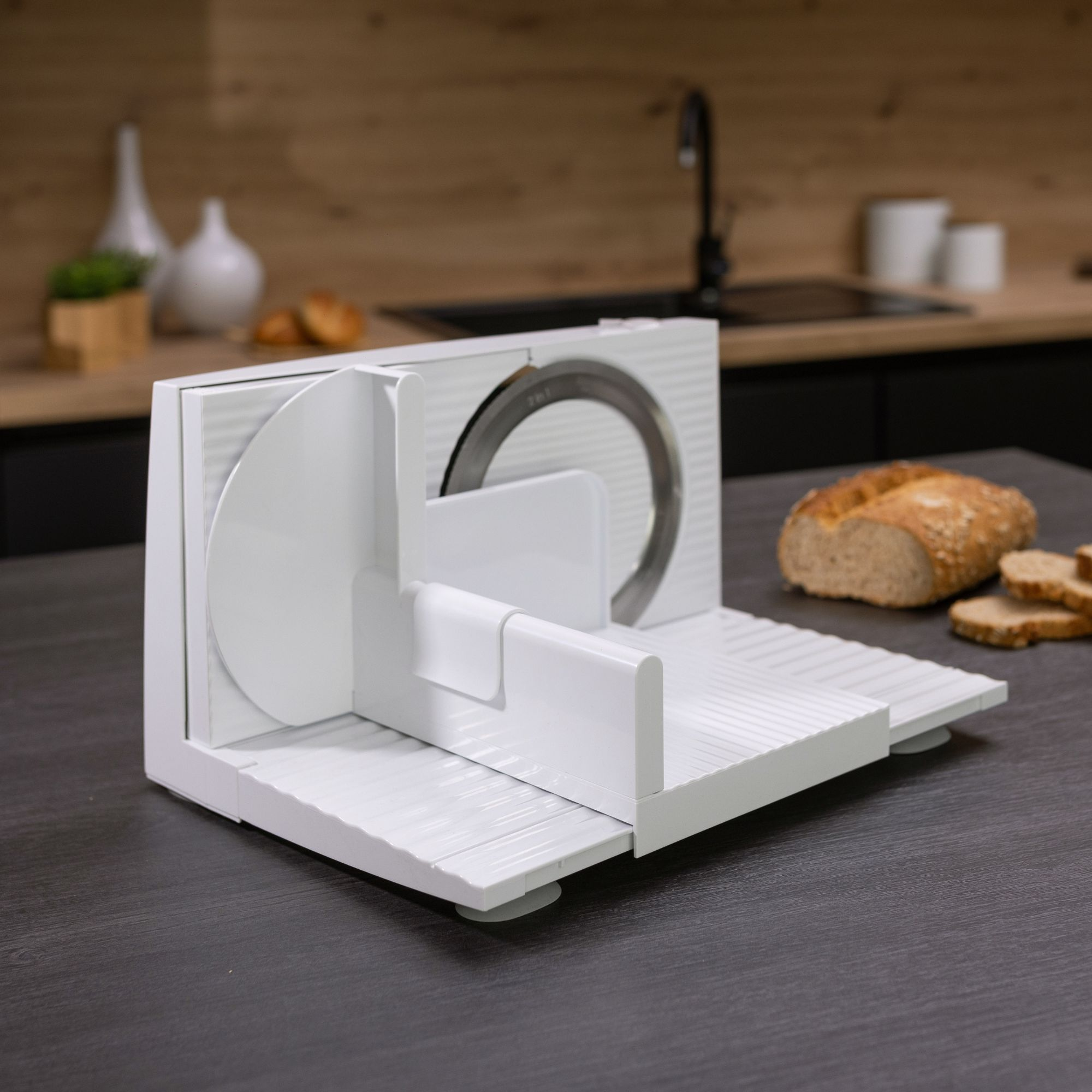 Eine weiße Fleischschneidemaschine auf einer Theke mit Brot und Küchenhintergrund.