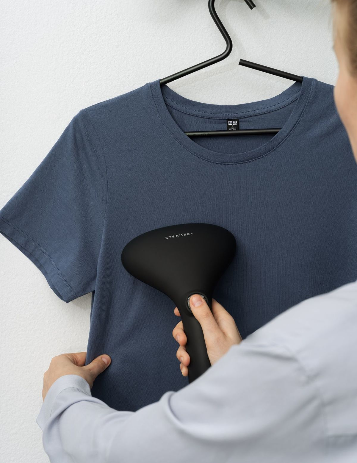 Person dampft ein blaues T-Shirt auf einem Bügel.