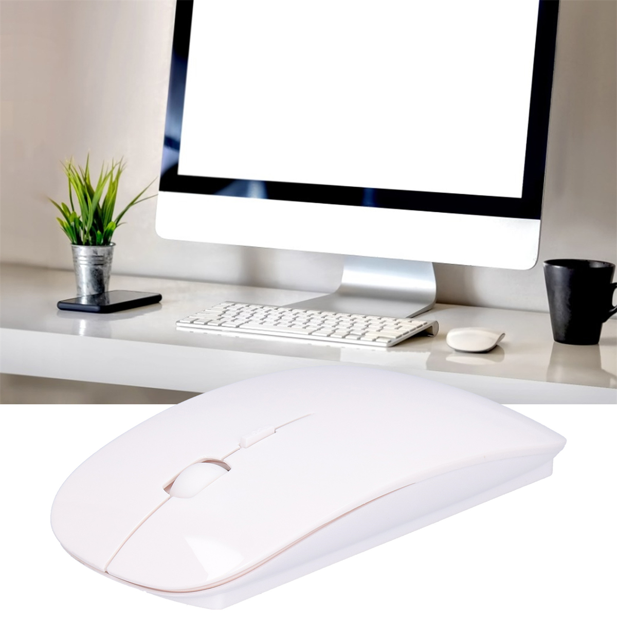 Weiße kabellose Maus auf einem Schreibtisch neben einer Tastatur, einem Monitor und einer schwarzen Tasse.