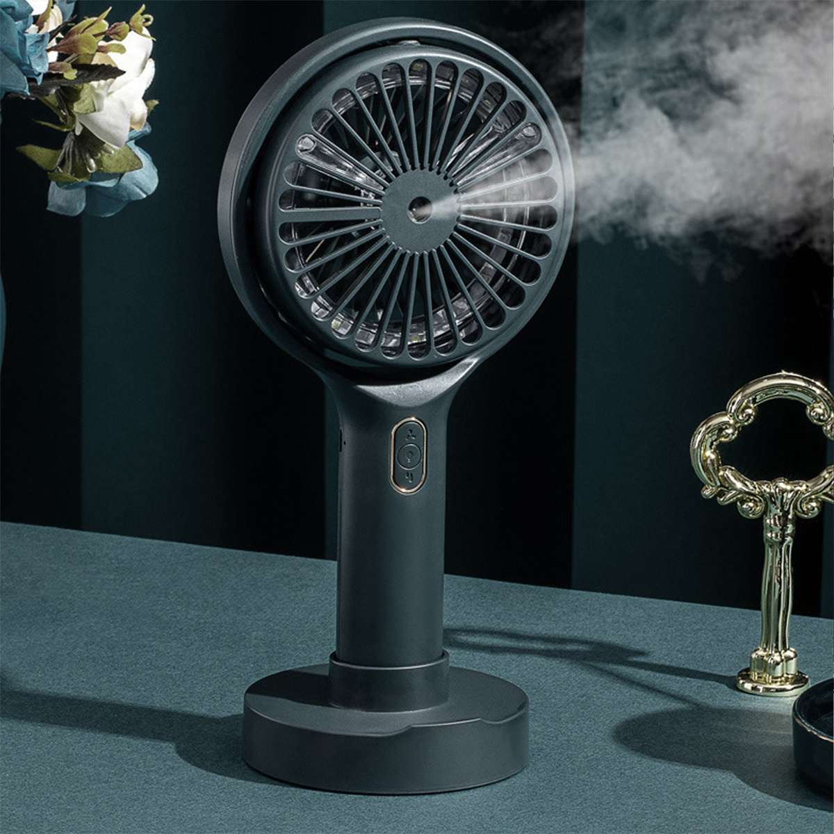 Kleiner, dunkelgrauer Ventilator auf einem Ständer. Er hat einen Griff und gibt Dampf ab. Ein Schlüssel und eine Oberfläche sind sichtbar.