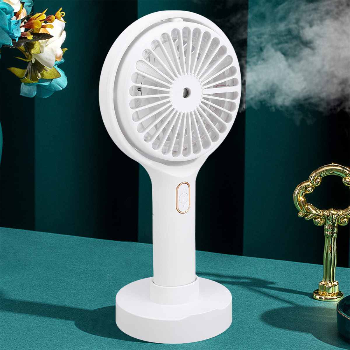Weißer Handventilator mit Ständer. Lüfterblätter sichtbar. Goldene Details am Griff. Türkisfarbene Oberfläche im Hintergrund.
