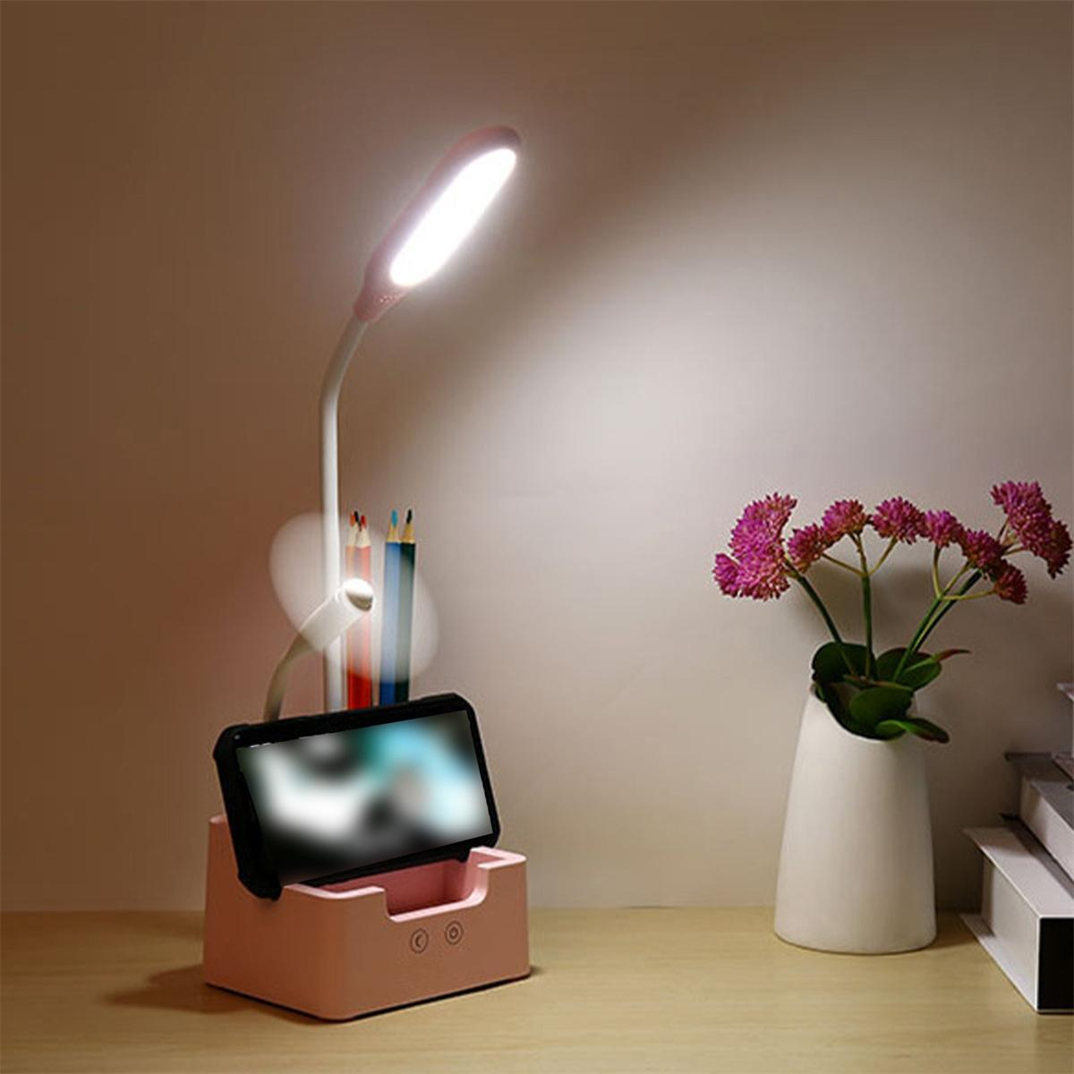 Rosa Schreibtischlampe mit Telefonhalter, Bleistiften und Vase mit Blumen.