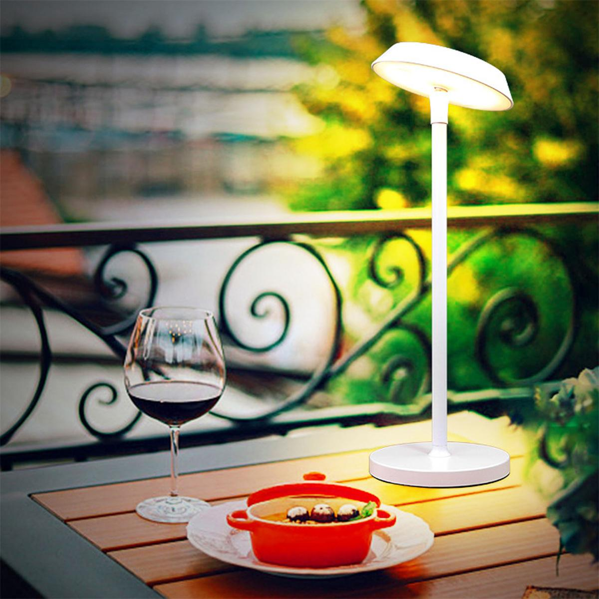 Weiße Tischlampe auf einem Holztisch mit einem Glas Wein und einem kleinen Gericht mit Essen.