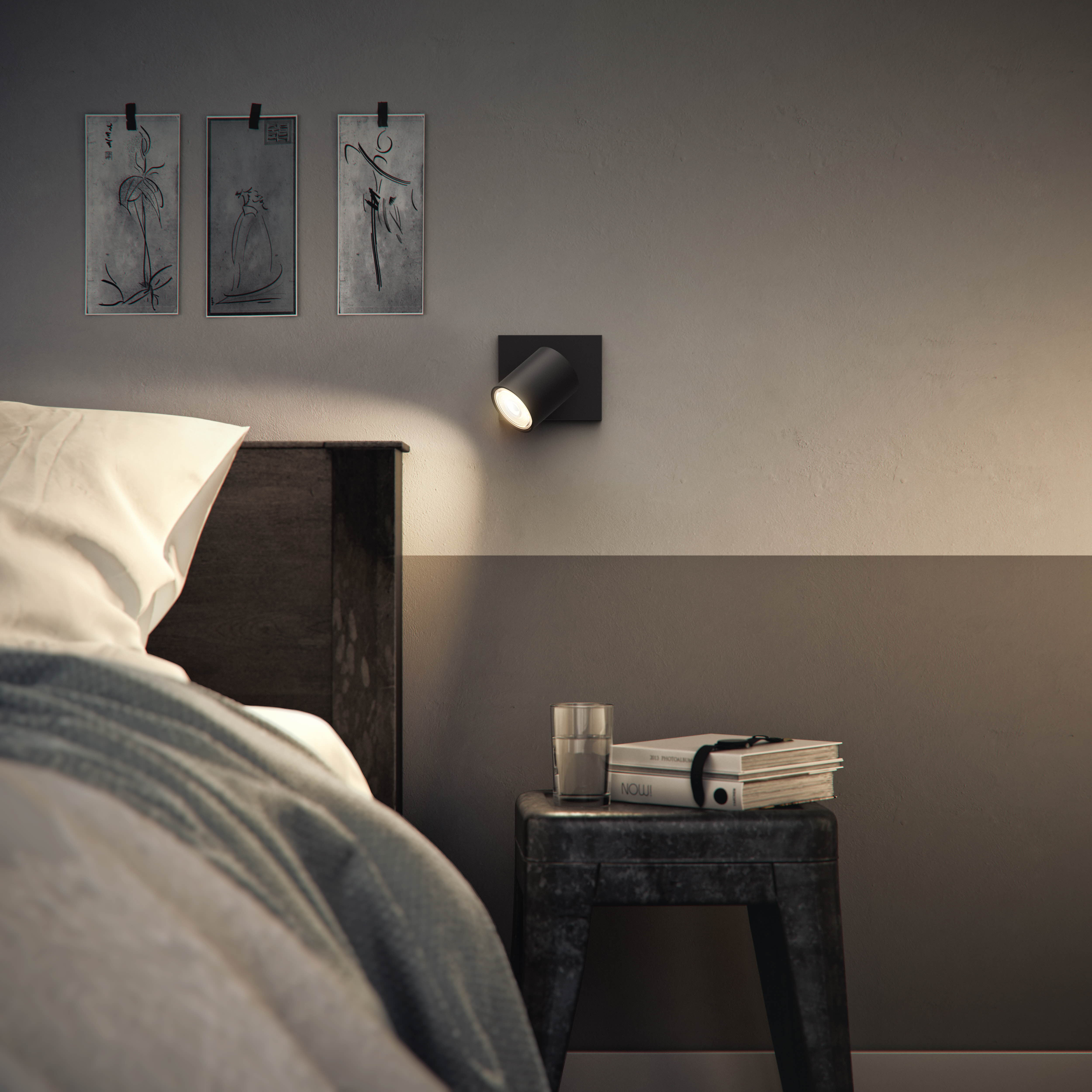 Schlafzimmer mit Kunst an der Wand und einer Leselampe. Es gibt ein Bett und einen Beistelltisch.