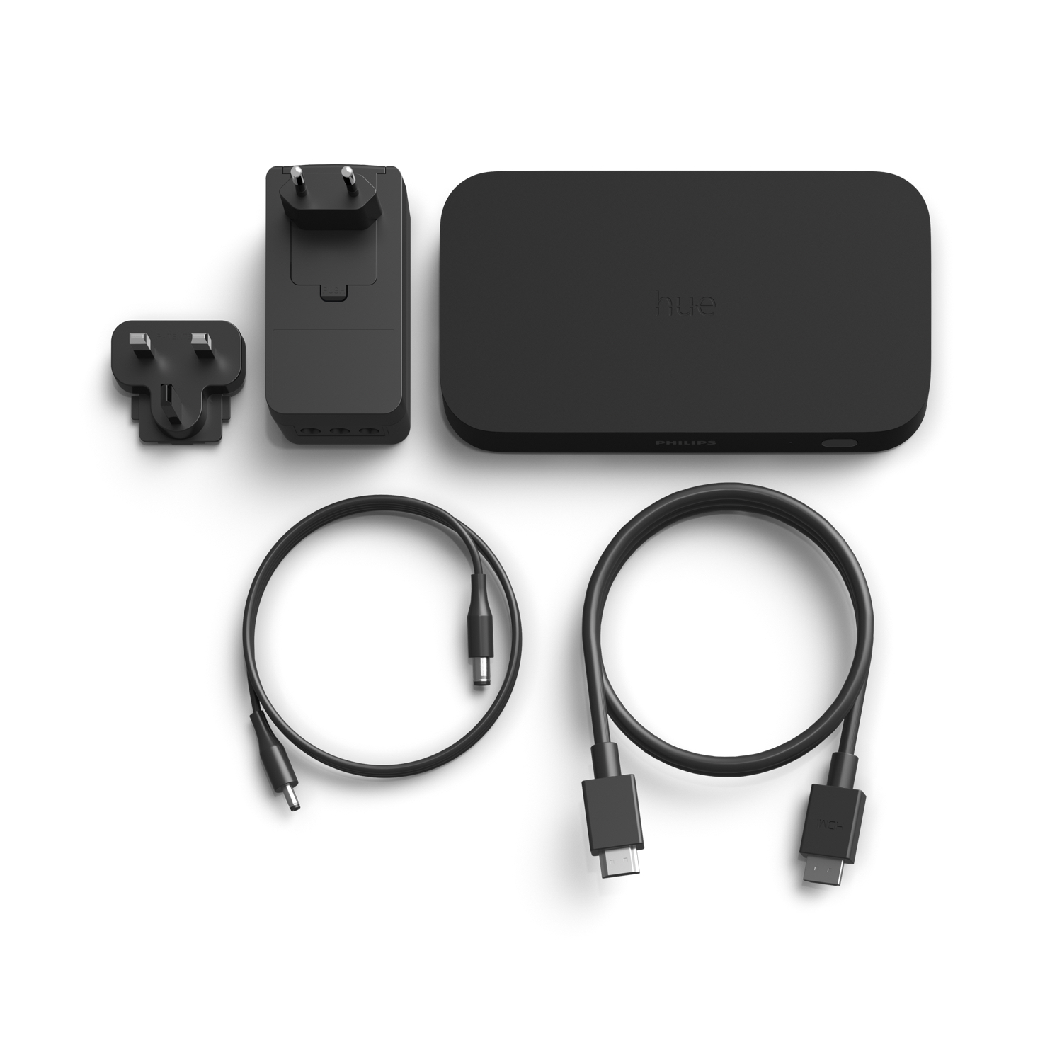 Disposición de adaptadores de corriente negros, cables y un dispositivo Philips Hue negro sobre un fondo blanco.