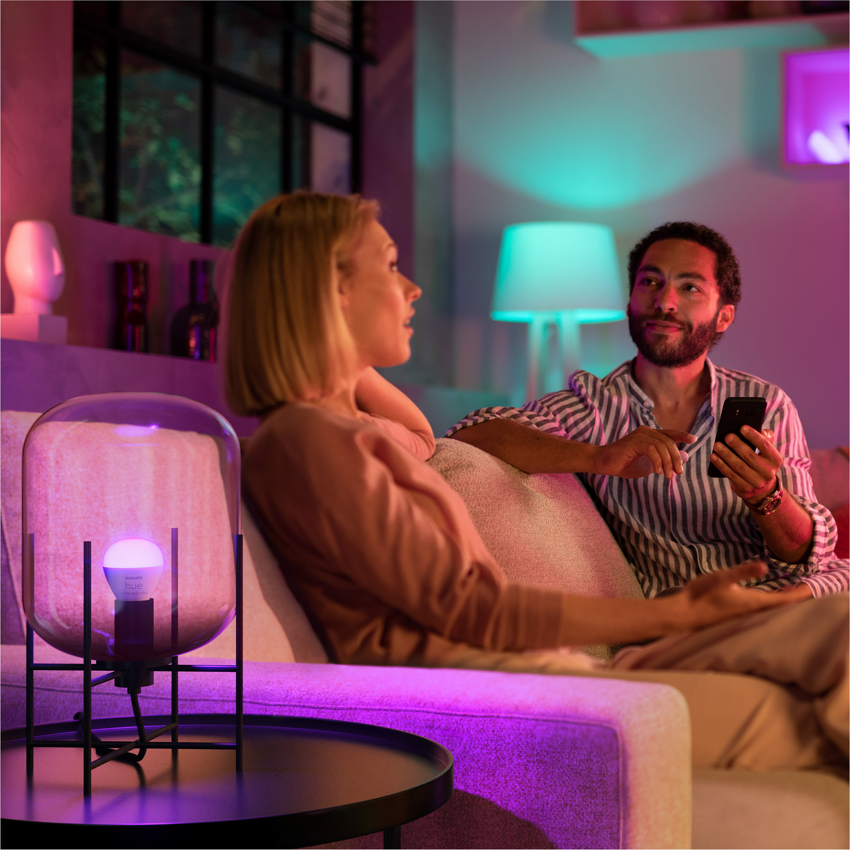 Paar sitzt auf einem Sofa. Lampe mit leuchtender Glühbirne links.