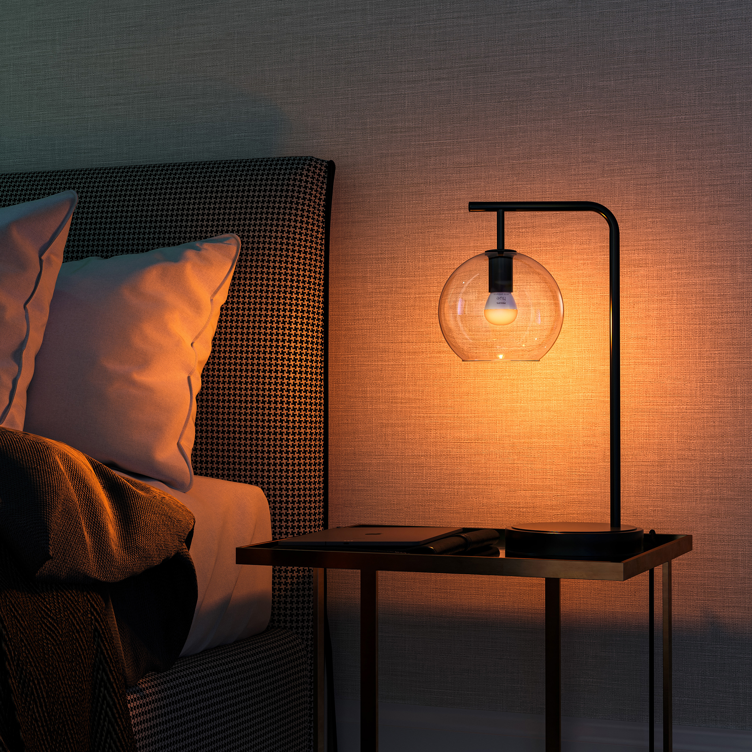 Eine Lampe mit einer kugelförmigen Glühbirne auf einem Tisch vor einem Bett.