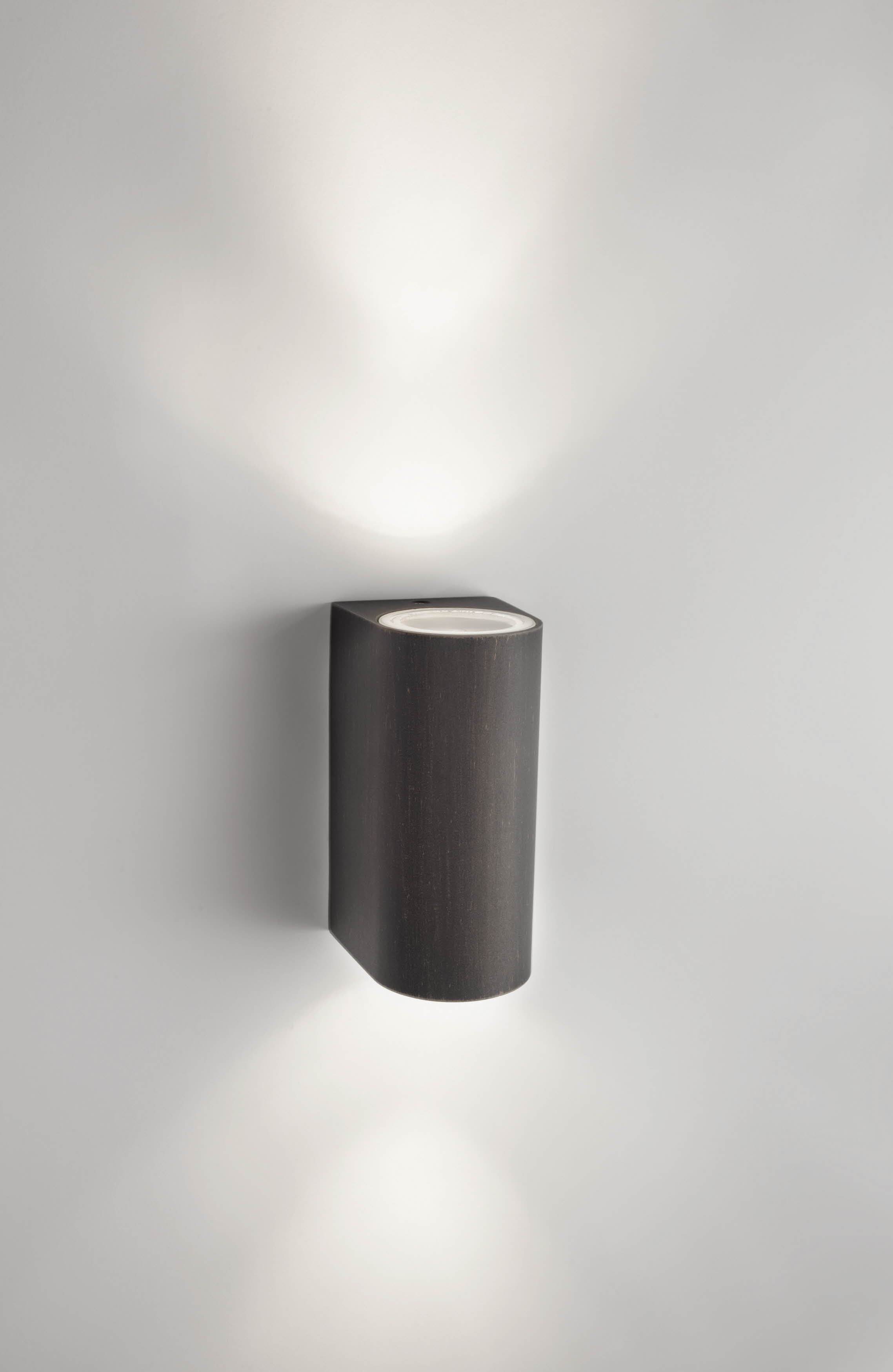 Eine schwarze Wandleuchte, die Licht nach oben und unten wirft, an einer weißen Wand.
