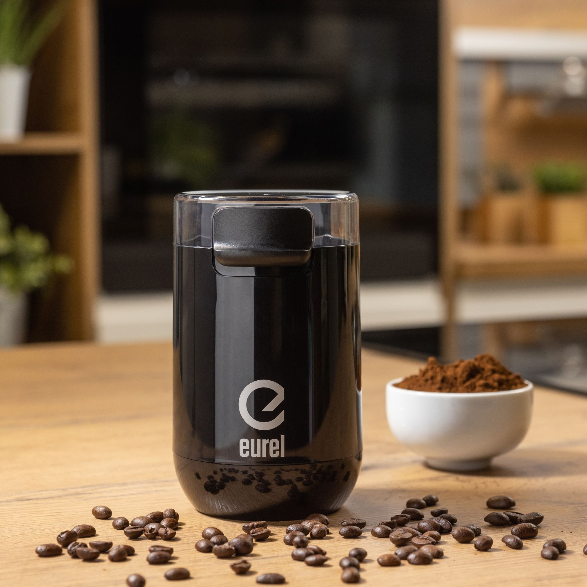 Eine schwarze Kaffeemühle, Kaffeebohnen und gemahlener Kaffee in einer weißen Schüssel.