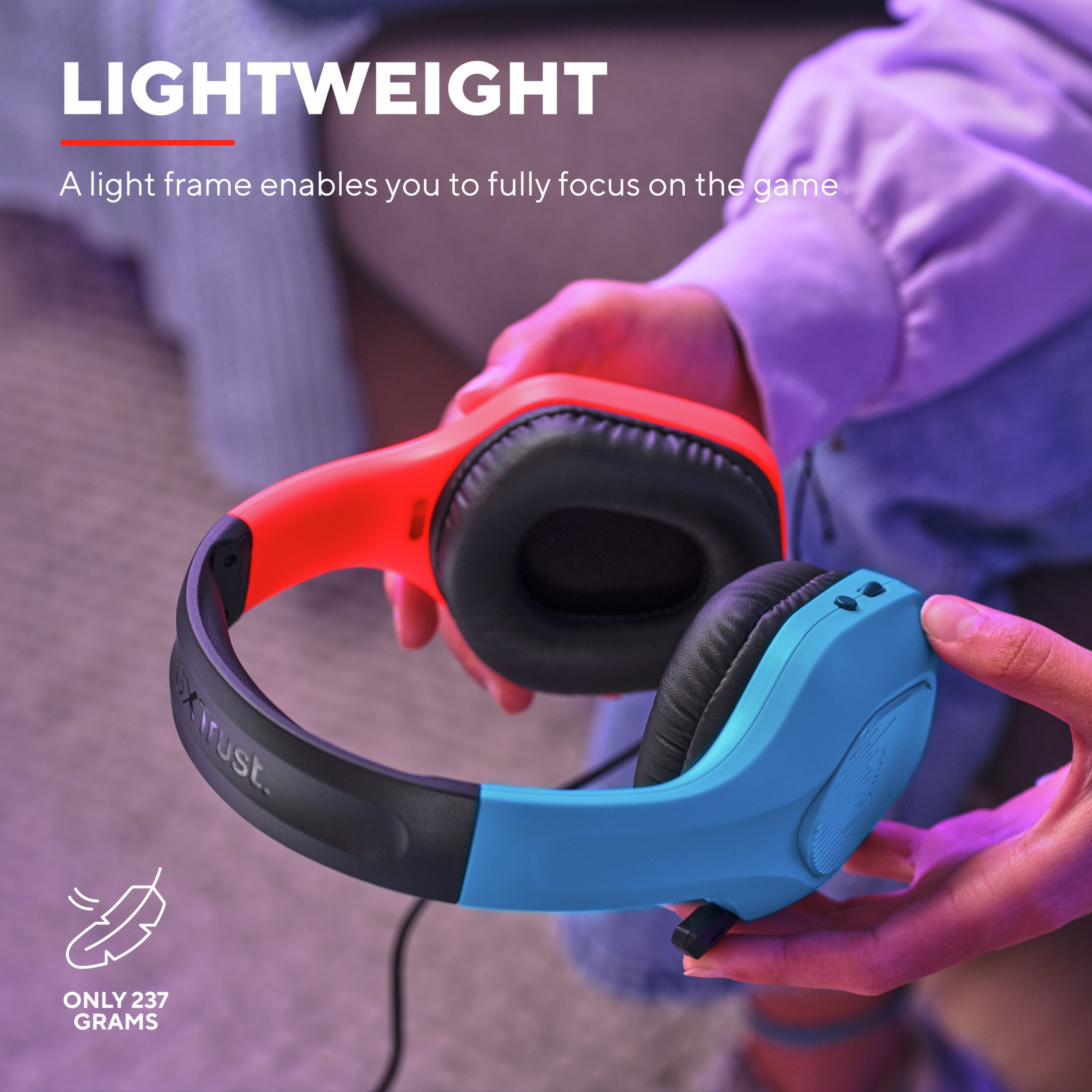 Osoba trzymająca pomarańczowe i niebieskie słuchawki. Tekst mówi 'Lekki' i 'Tylko 237 gramów'.