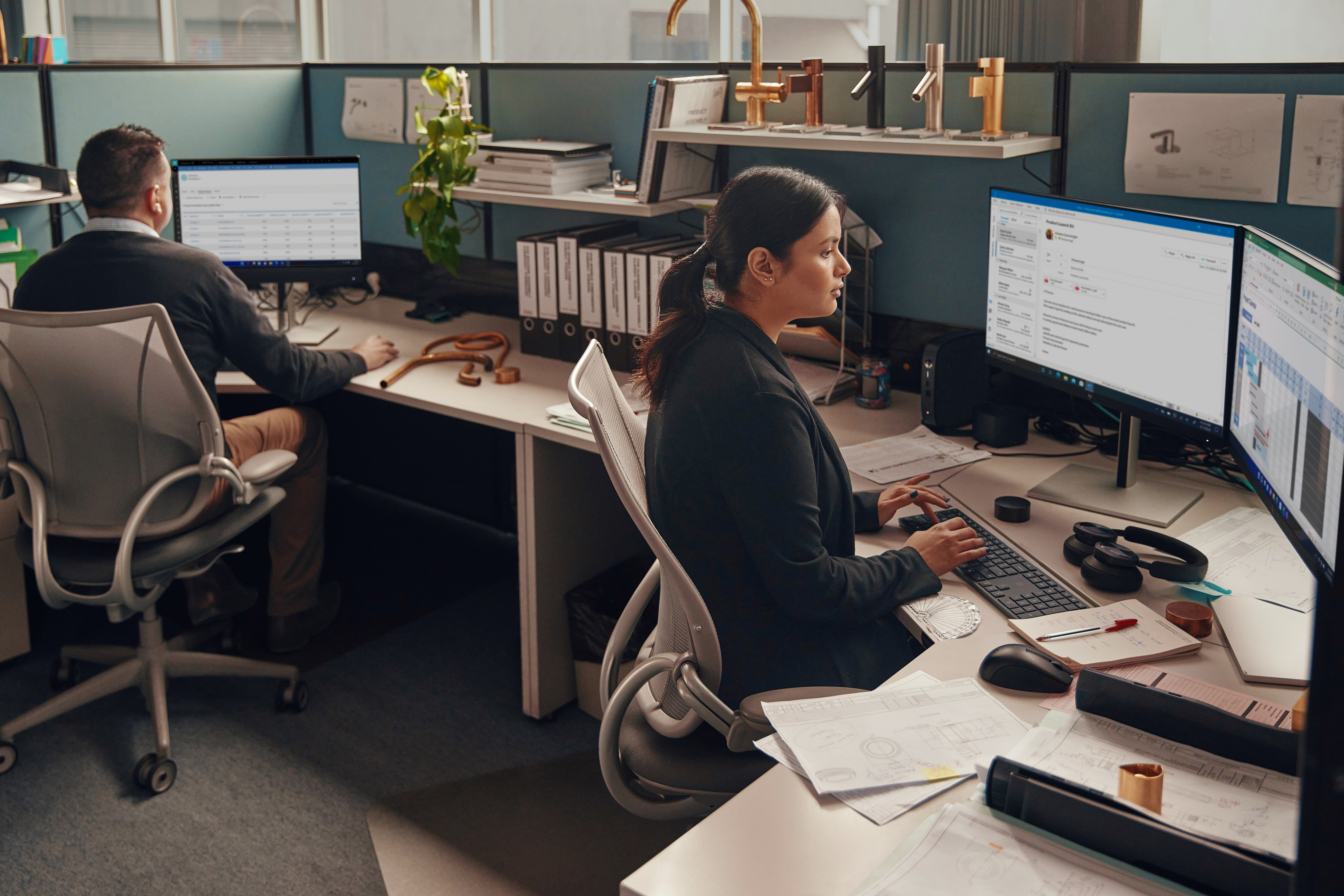 Ambiente d'ufficio con due persone che lavorano alle scrivanie, con computer e forniture per ufficio.