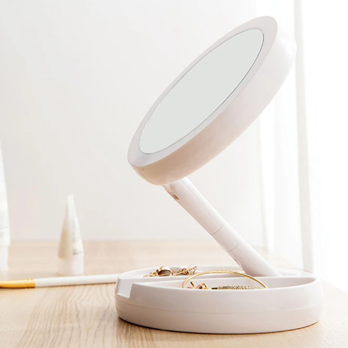 Espejo blanco plegable con bandeja. Joyas y maquillaje en la mesa en primer plano.