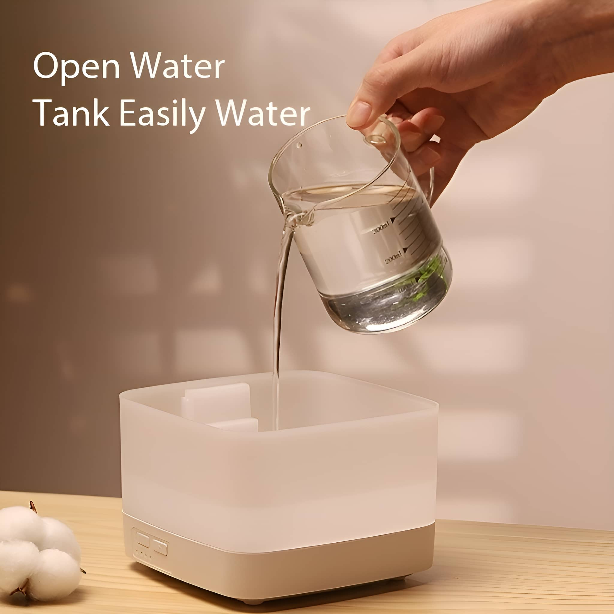 Hand gießt Wasser aus Becherglas in weißen, quadratischen Wassertank. Watte sichtbar.