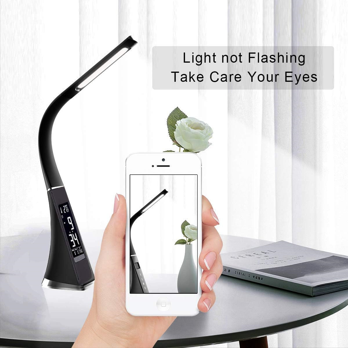 Eine schwarze Schreibtischlampe mit Digitalanzeige. Eine Hand hält ein Smartphone mit der Lampe.