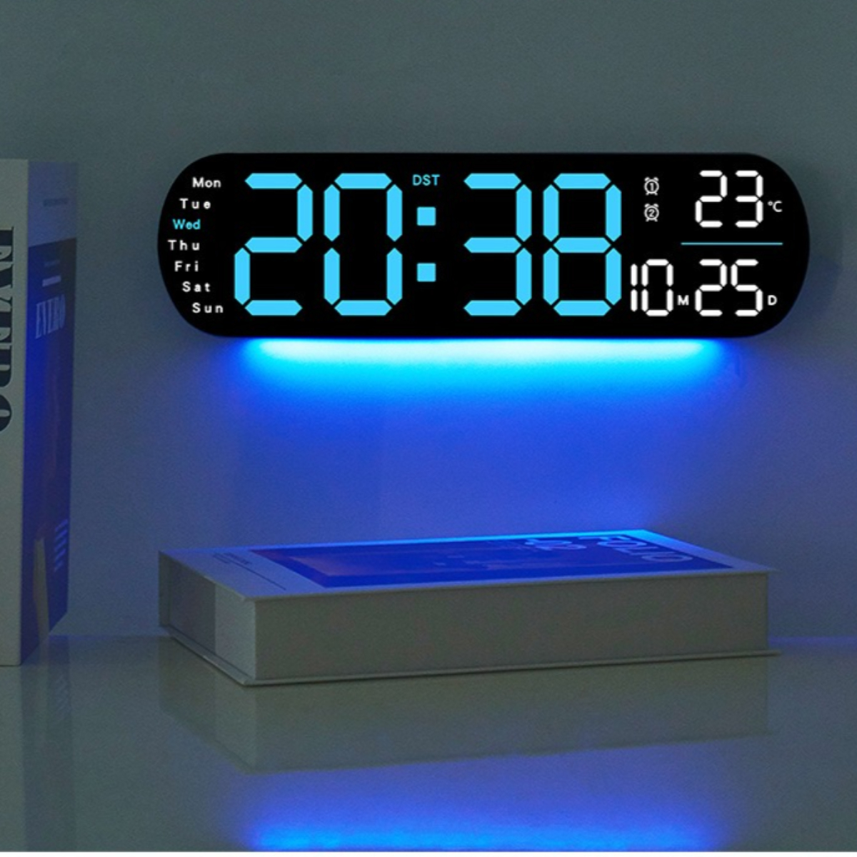 Digitaluhr mit großen blauen Ziffern, zeigt Zeit und Datum. Auf einem weißen Regal platziert.