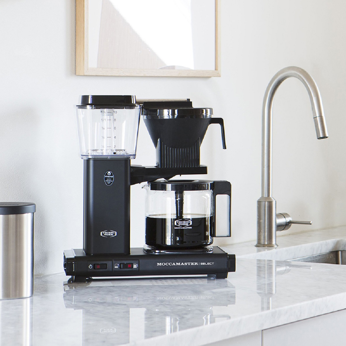 Czarny ekspres do kawy ze szklaną karafką. Urządzenie stoi na białej marmurowej powierzchni.