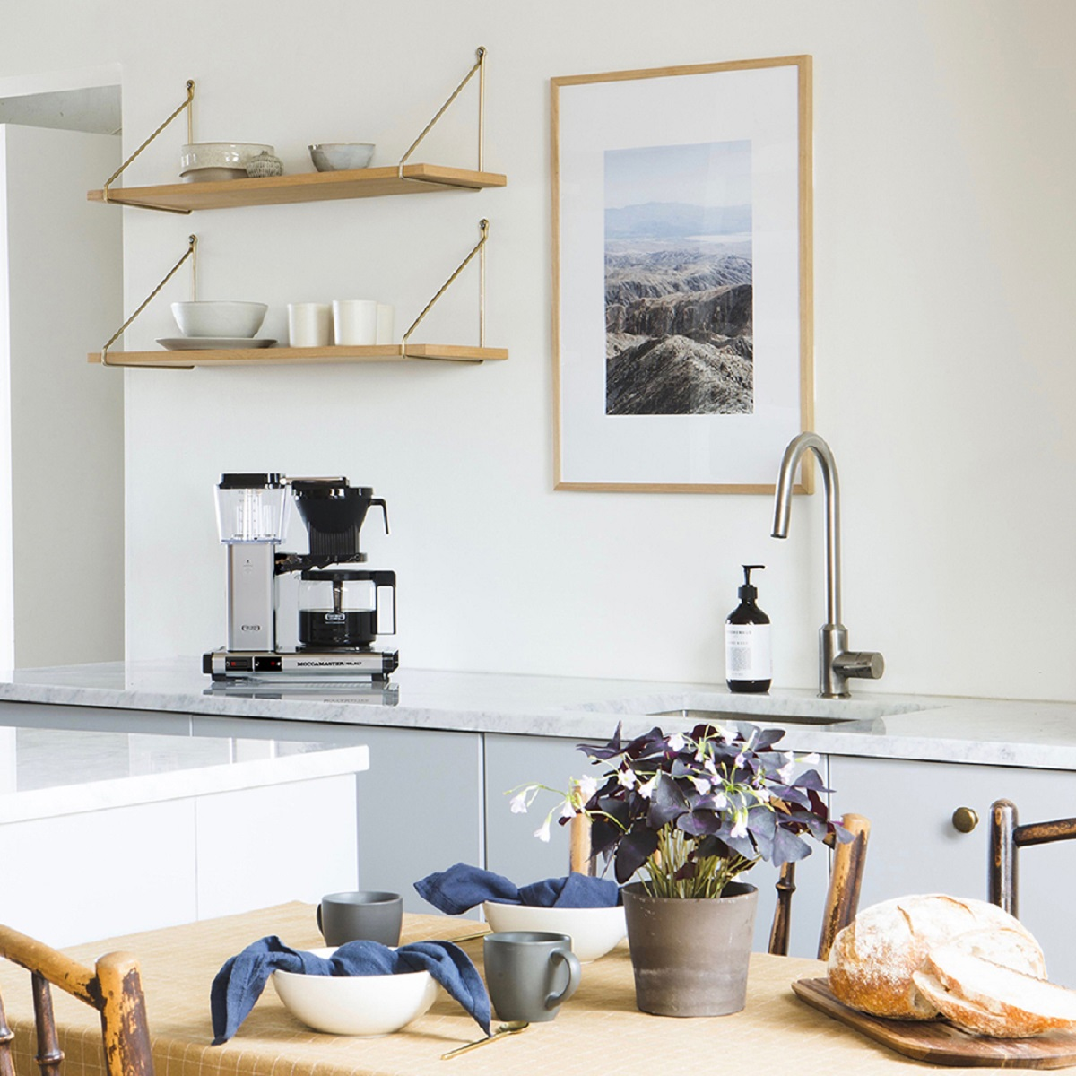 Keuken met planken, koffiezetapparaat, gootsteen, foto en brood op tafel.