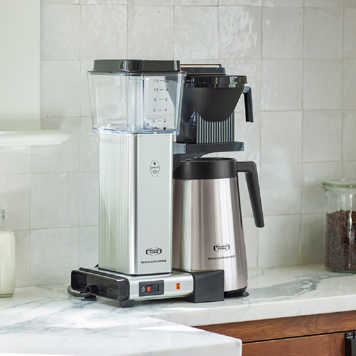 Eine silberne und schwarze Kaffeemaschine mit einer Glaskaraffe und einer Thermokaraffe. Sie steht auf einer Marmorarbeitsplatte.