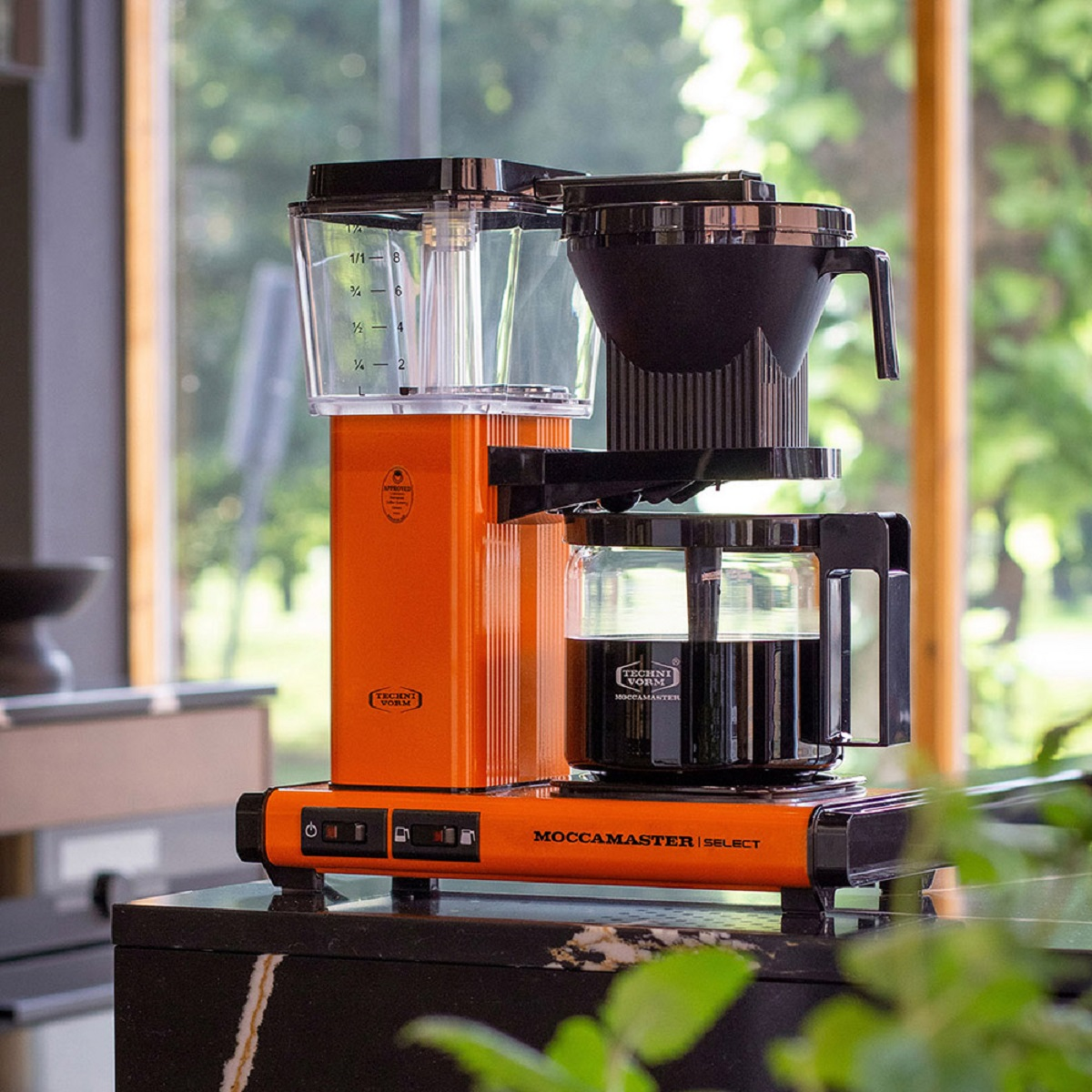 Een oranje Moccamaster koffiezetapparaat op een aanrecht. Zwarte en glazen componenten zijn zichtbaar.