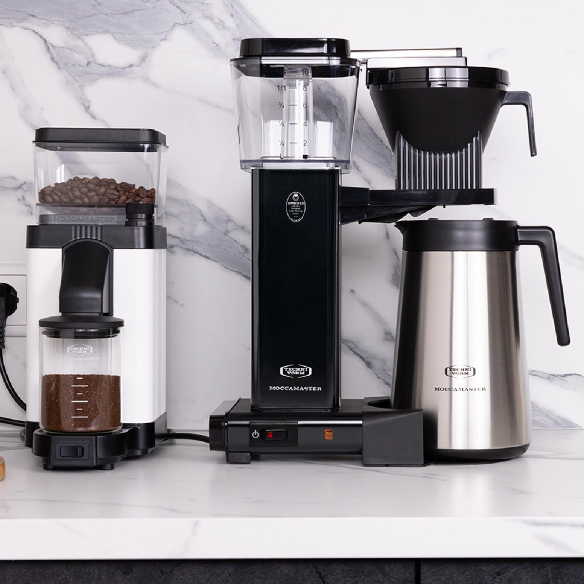 Kaffeemaschine mit schwarzen und Edelstahlkomponenten, Kaffeemühle und Kaffeebohnen auf Theke.