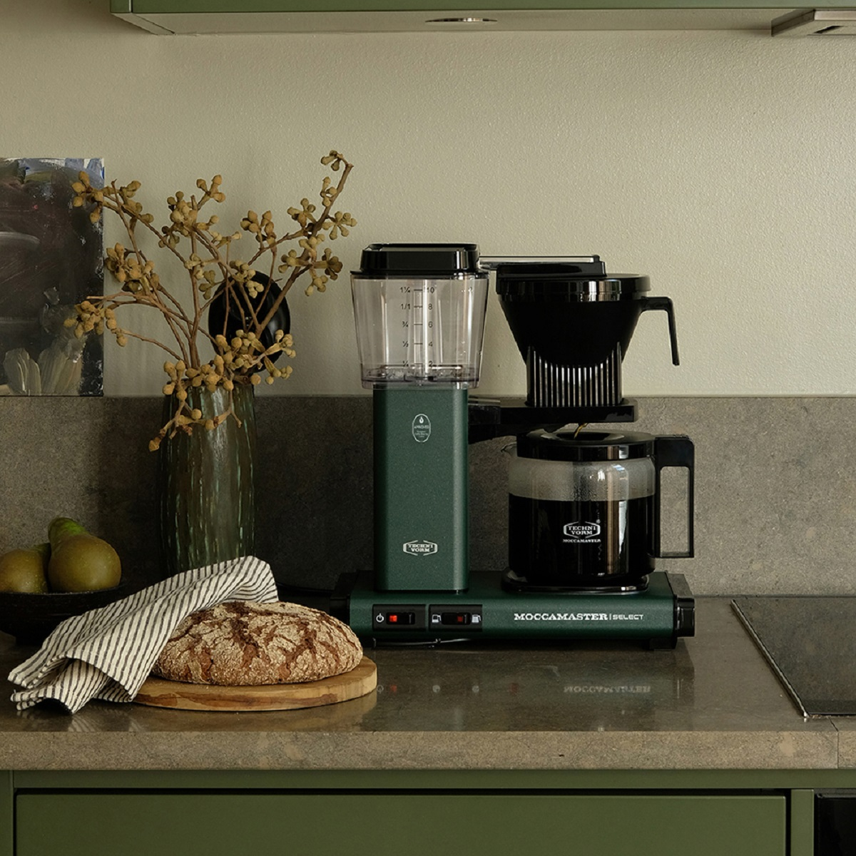 Keuken met een groene koffiemachine, brood, peren en vaas.