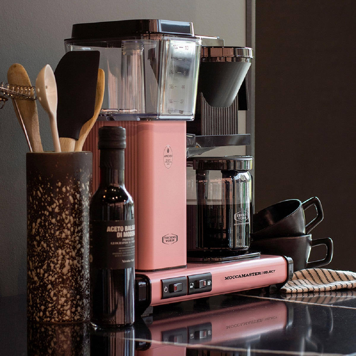 Pink coffee maker with accessories on a counter.