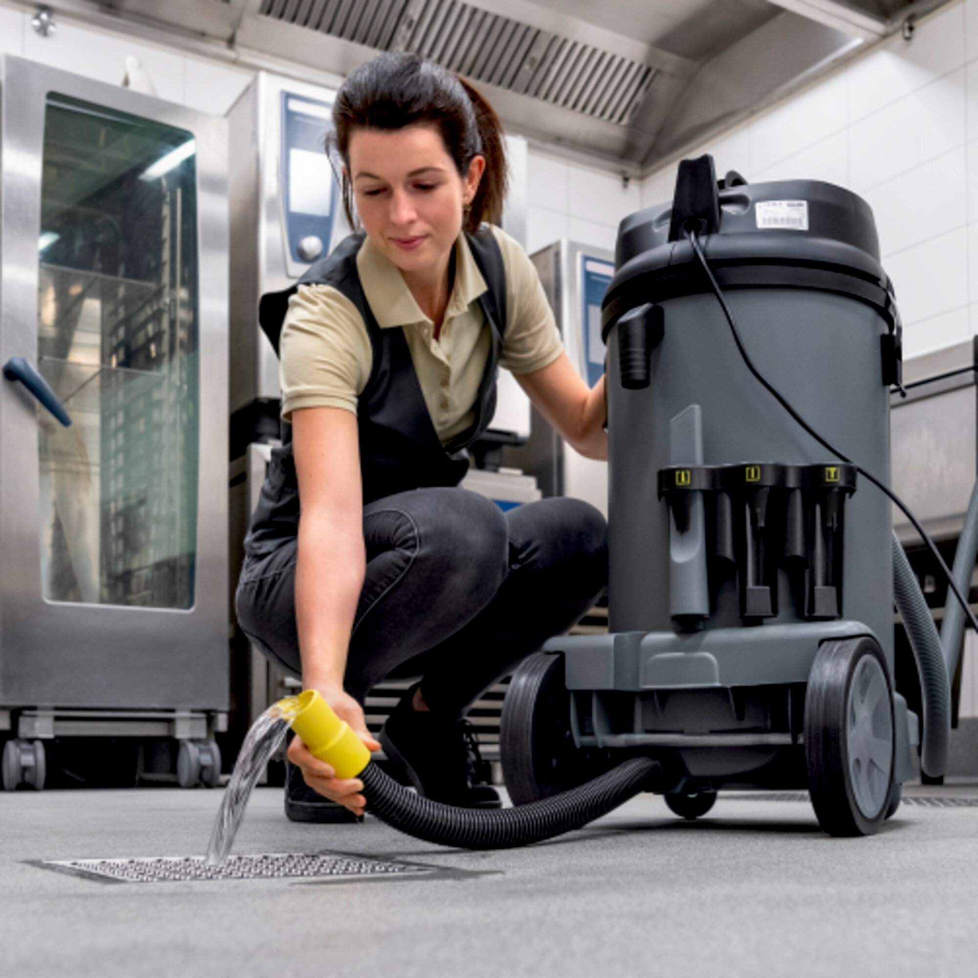 Une femme nettoie le sol avec un aspirateur. La femme est dans une cuisine.