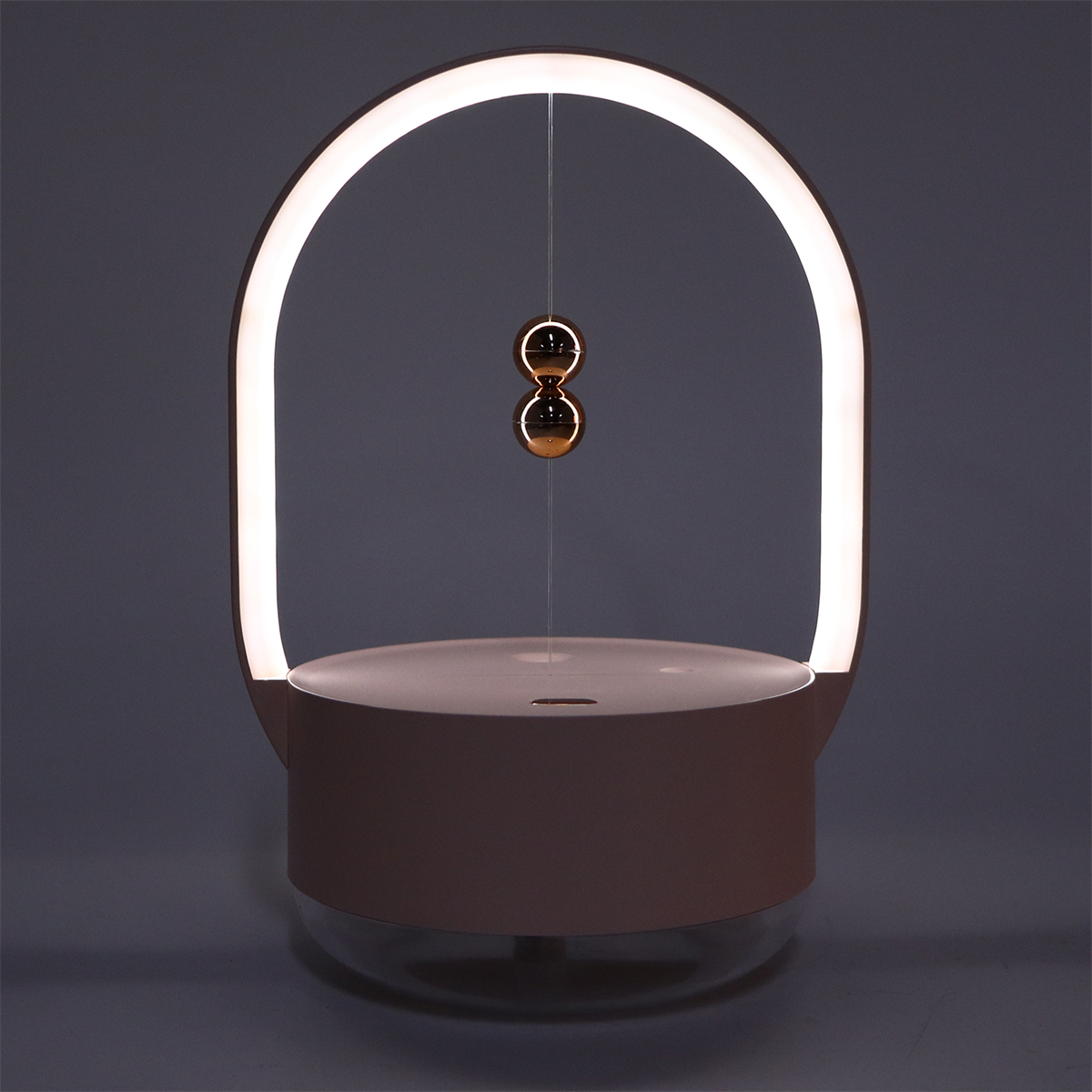 Eine dekorative Lampe mit zwei goldenen Kugeln, die hängen, und einem bogenförmigen Licht oben. Die Basis ist rosa.