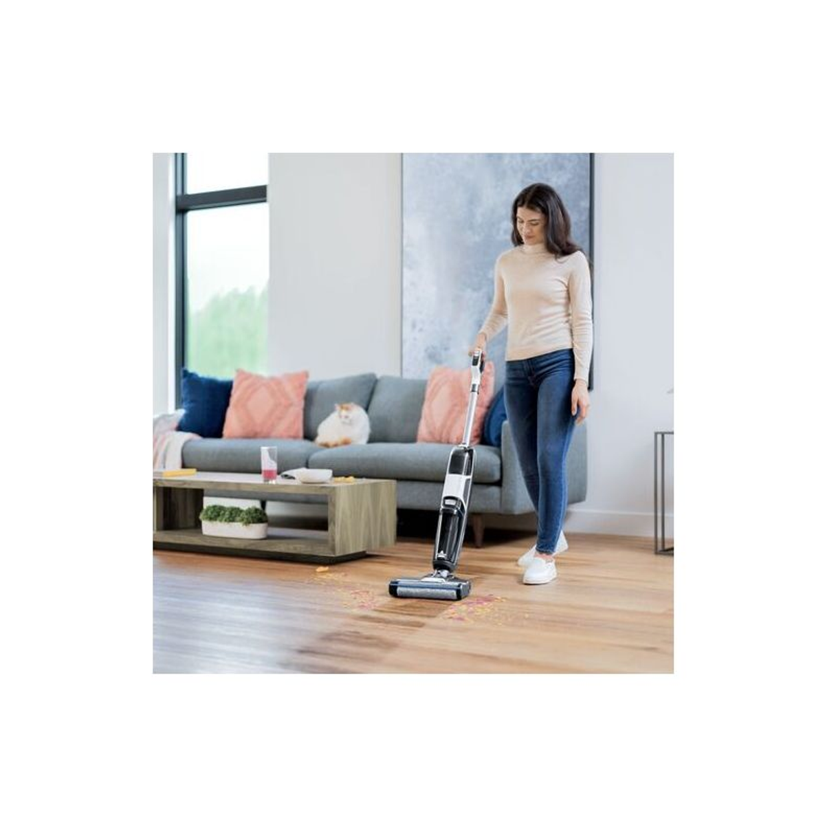A woman vacuuming a wooden floor with a cordless vacuum cleaner in a living room.