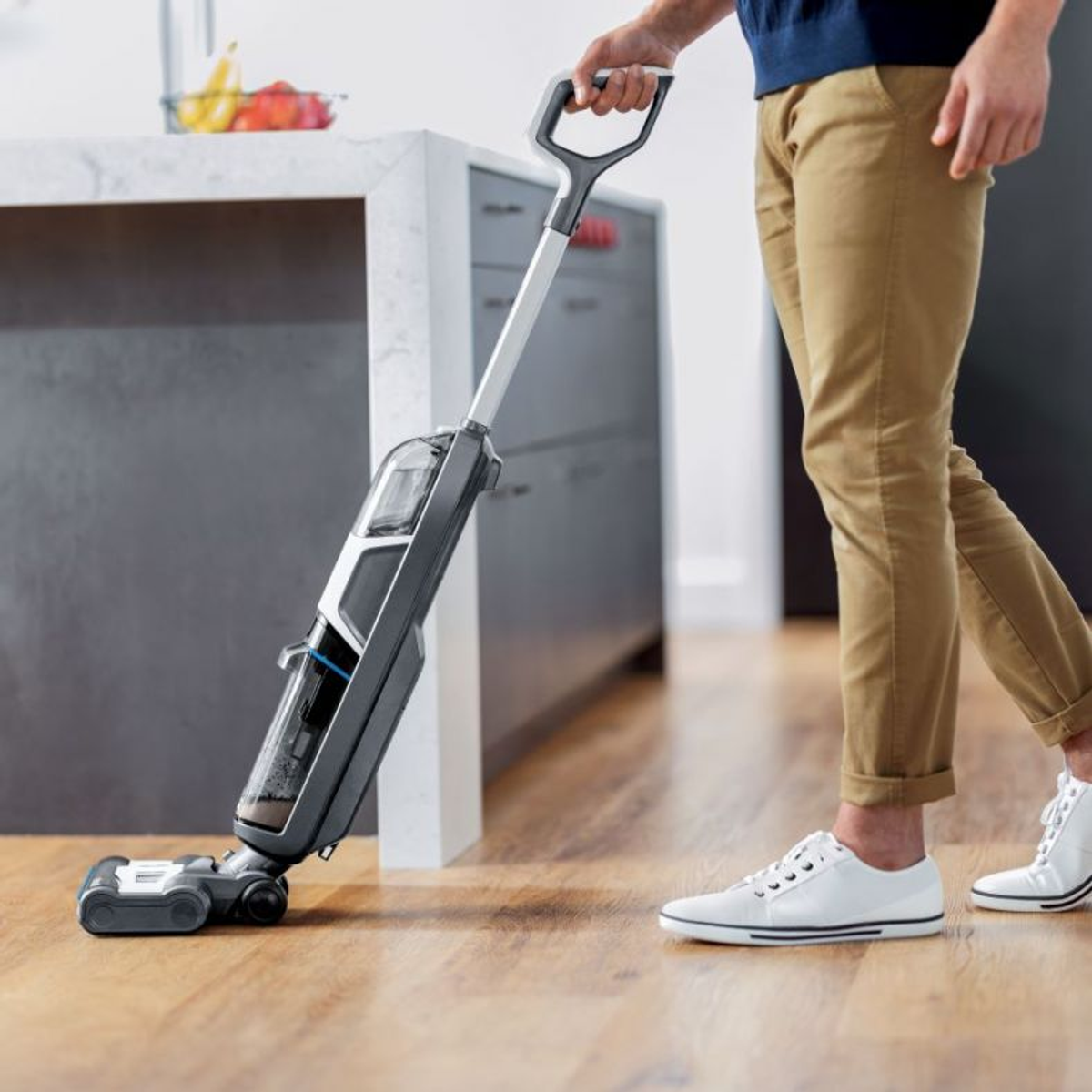 A person using a floor cleaning machine on wood flooring. The person is wearing a blue shirt and khaki pants.