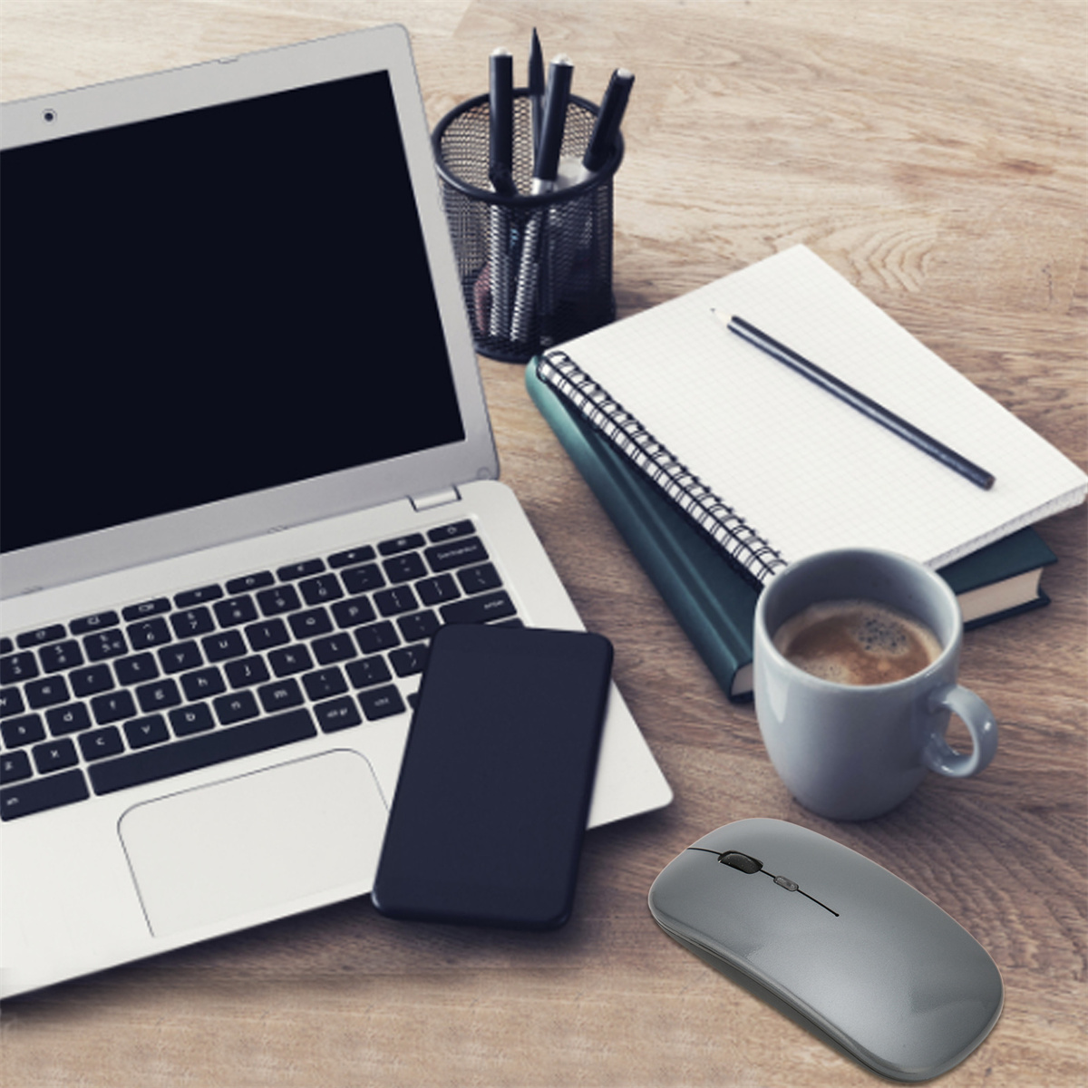 Ein Laptop, Telefon, Notizbuch, Bleistift, Kaffee und eine Maus auf einem Holztisch. Die Maus ist grau.