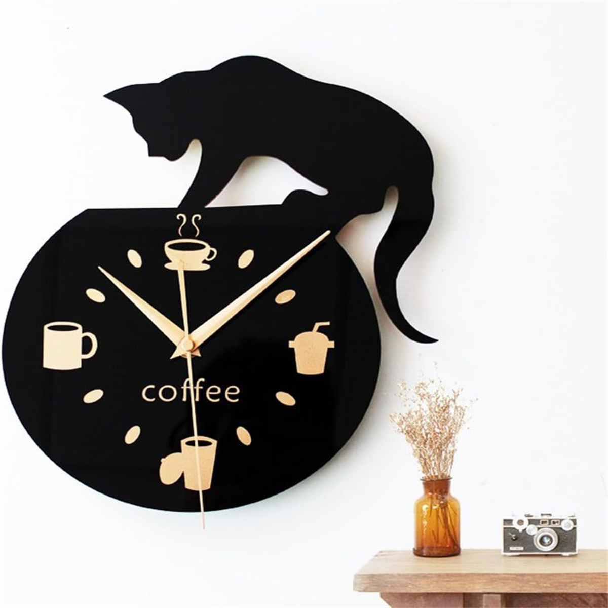 Schwarze Katzenuhr mit Kaffee-Symbolen, Vase und Kamera auf einem Tisch.