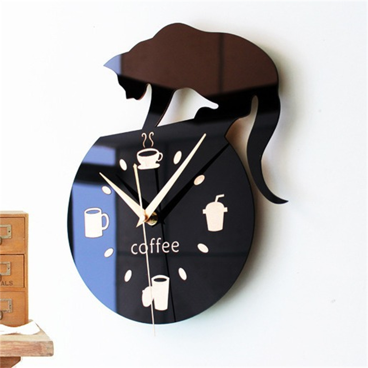 Schwarze katzenförmige Uhr. Die Uhr hat kaffeebezogene Symbole. Die Wand ist weiß. Es gibt kleine Schubladen.
