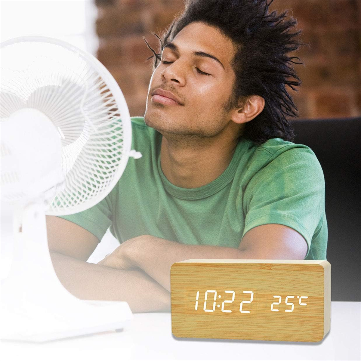 Ein Mann entspannt sich vor einem Ventilator, während eine Holzuhr Zeit und Temperatur anzeigt.