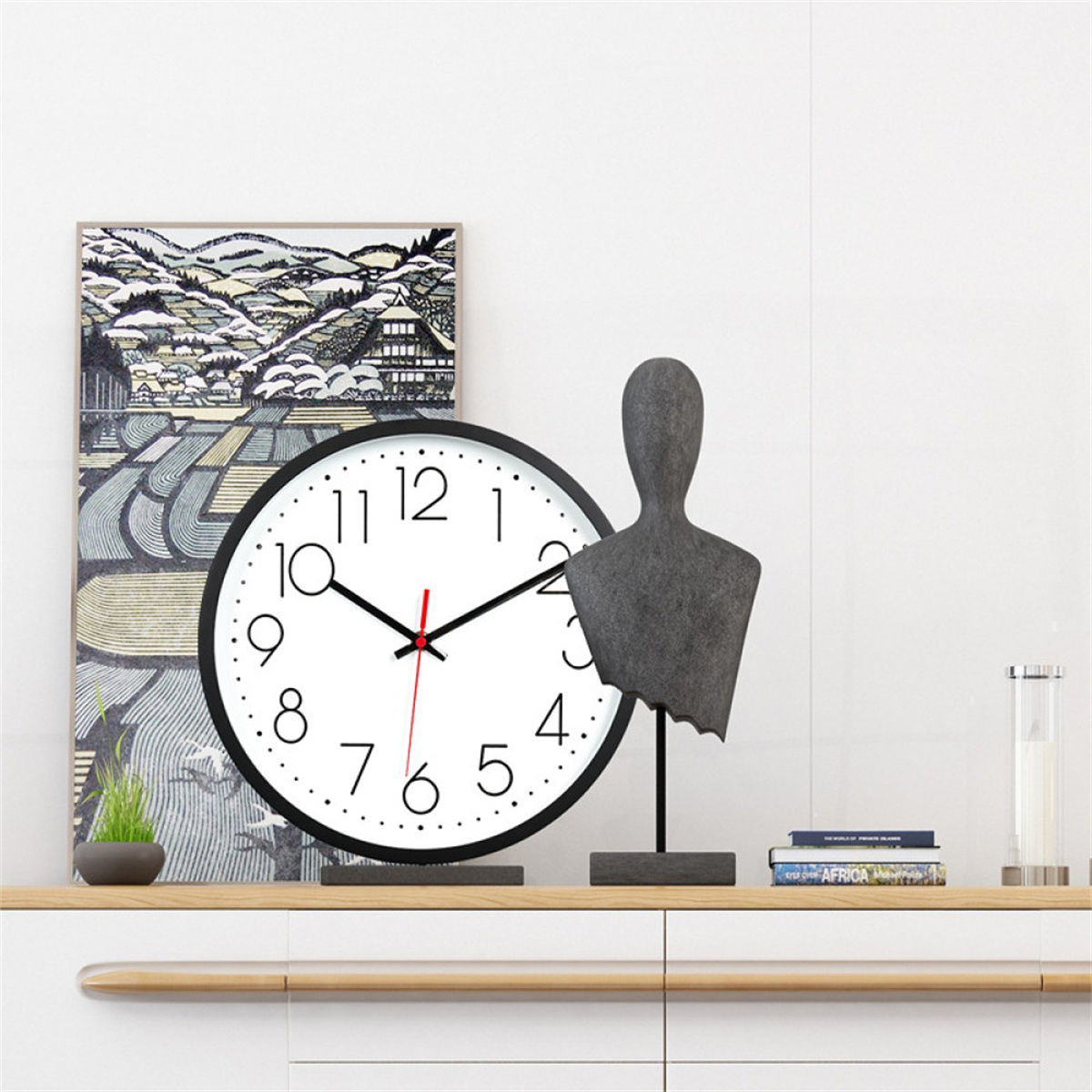 Eine Uhr, eine Statue und ein Gemälde stehen auf einem weißen Regal. Die Uhr ist schwarz.