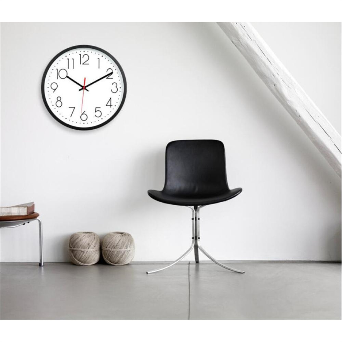 Eine schwarze Uhr an einer weißen Wand, mit einem schwarzen Stuhl und einem kleinen Tisch.
