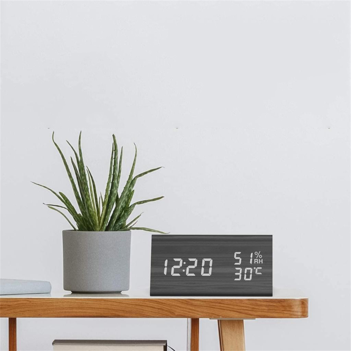 Digitaluhr auf einem Tisch mit einer Pflanze. Weißer Wandhintergrund.