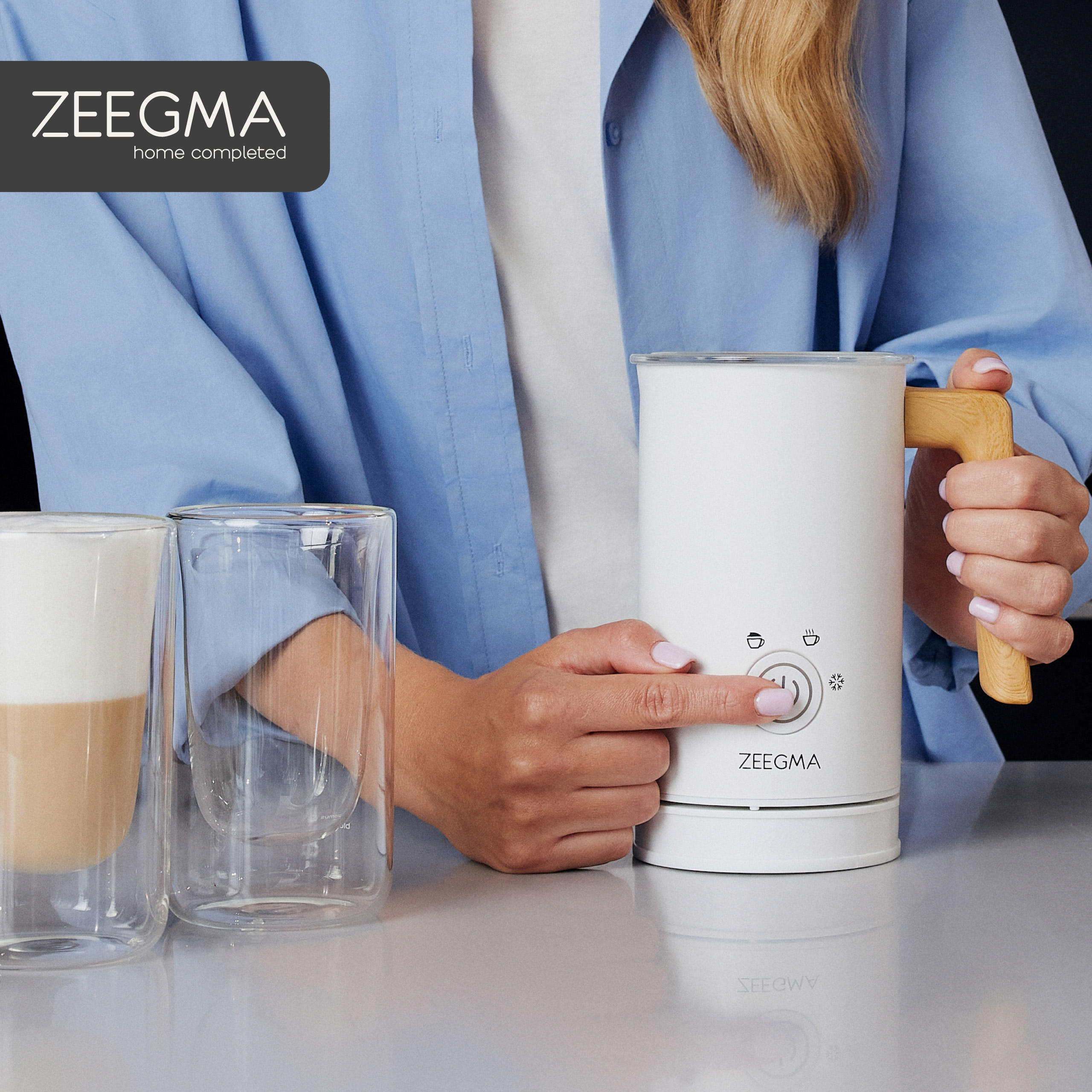 Kobieta obsługująca biały spieniacz do mleka. Zawiera szklanki i latte.