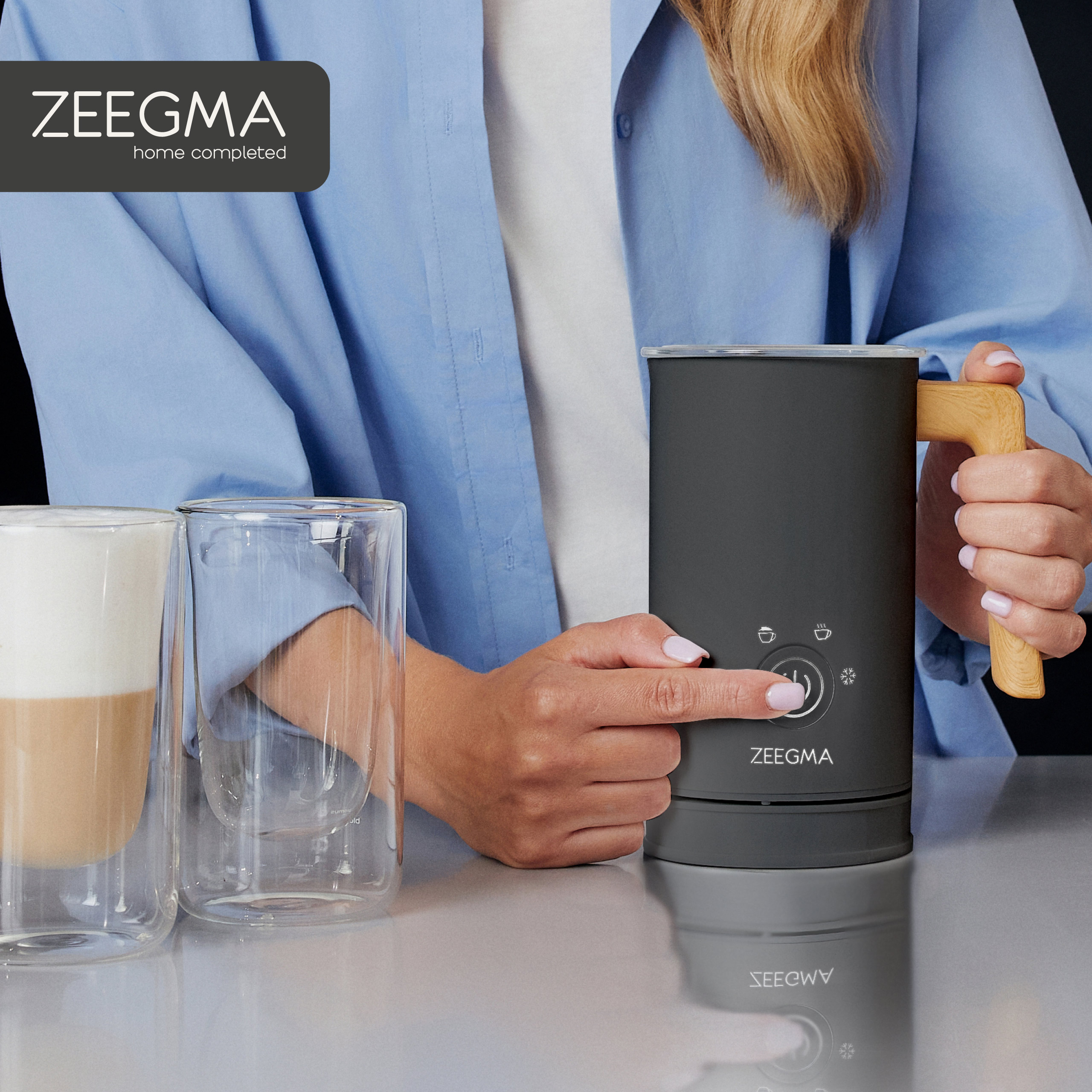 Kobieta naciska przycisk spieniacza do mleka, dwa szklanki w kadrze.