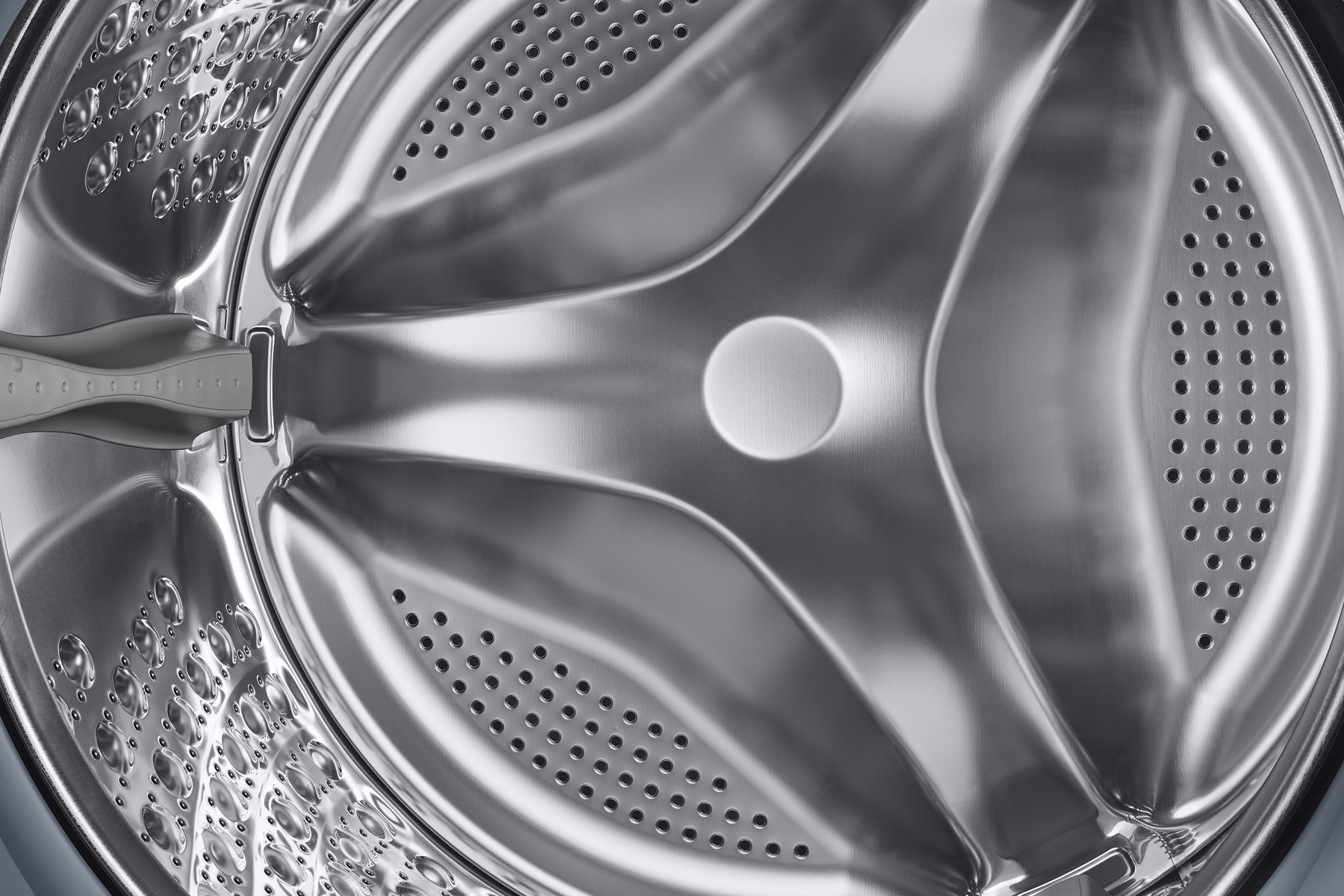 Wnętrze bębna pralki, błyszczący metal, z otworami i centralną piastą.