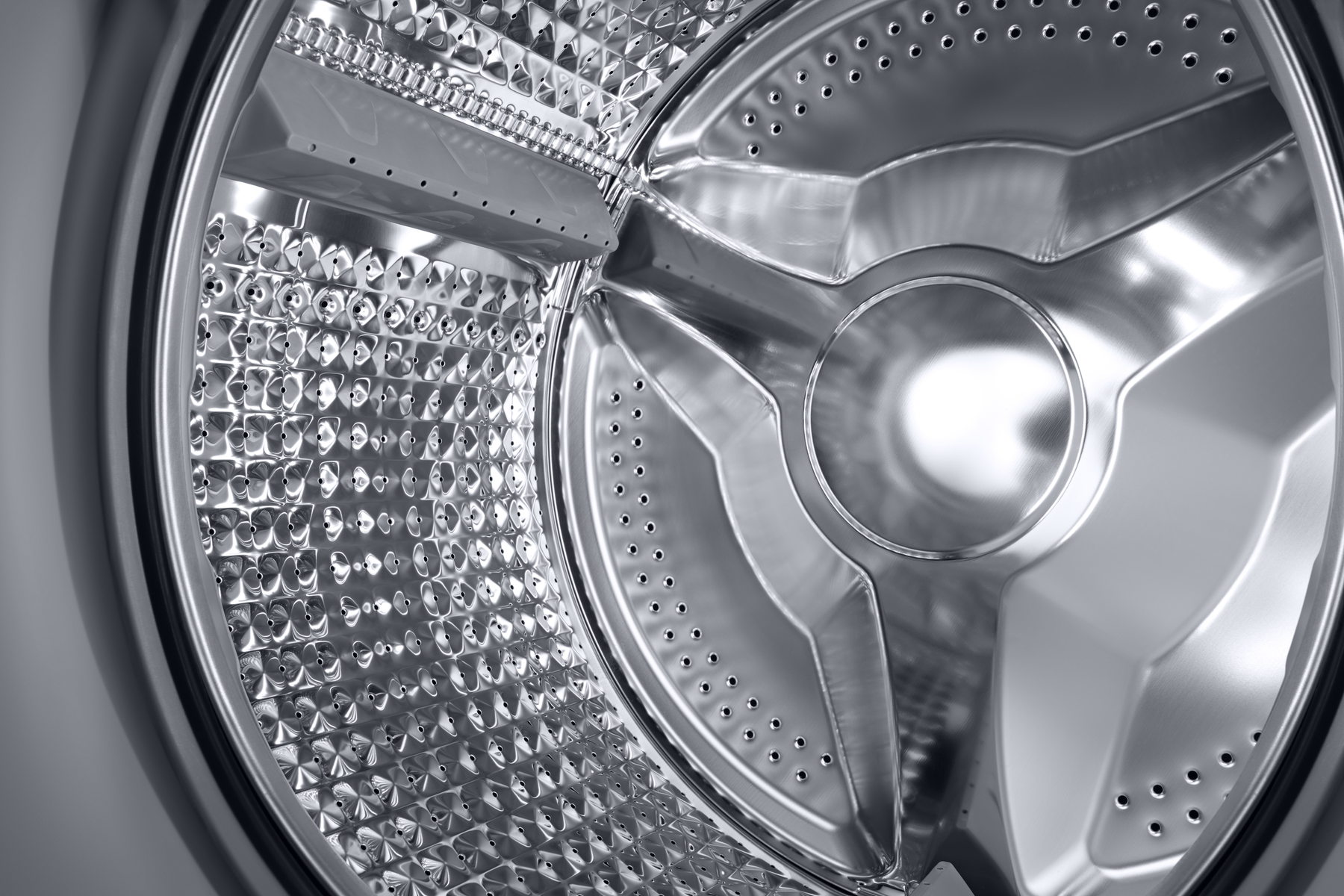 Zbliżenie błyszczącego, perforowanego bębna pralki ze stali nierdzewnej.
