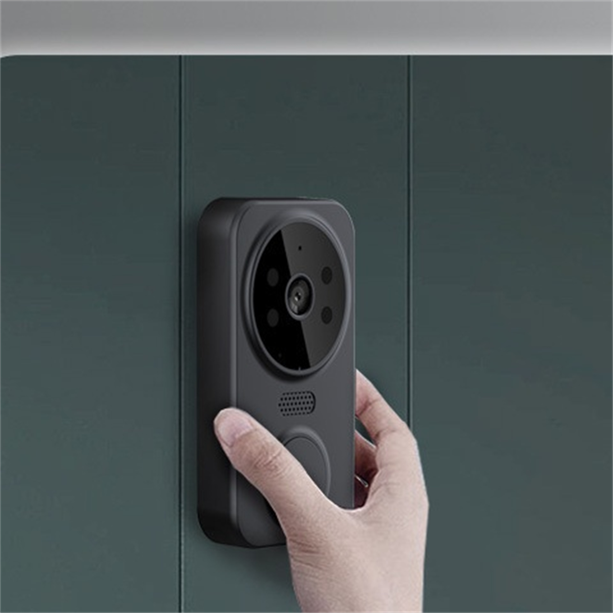 Eine schwarze Türklingel an einer grünen Wand, eine Hand drückt einen Knopf.